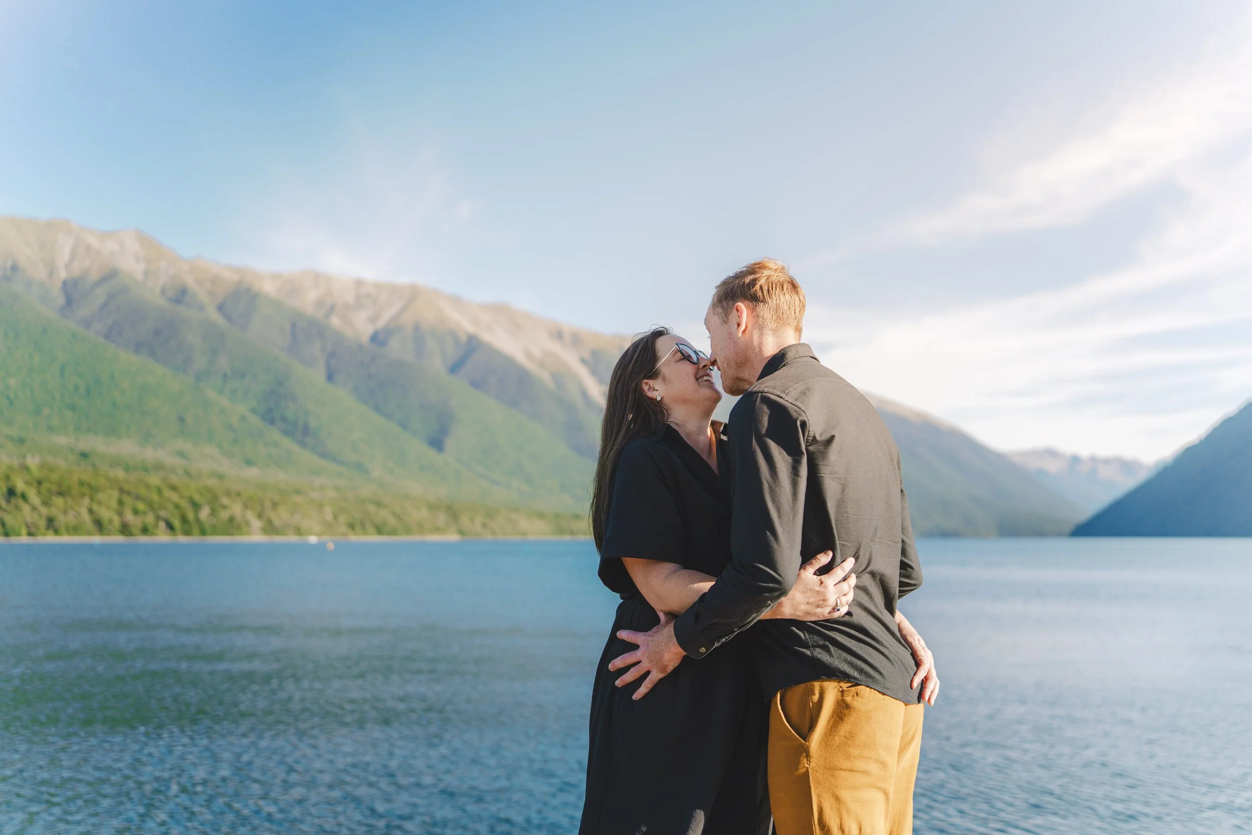 A couple embracing by a lake with mountains in the background
