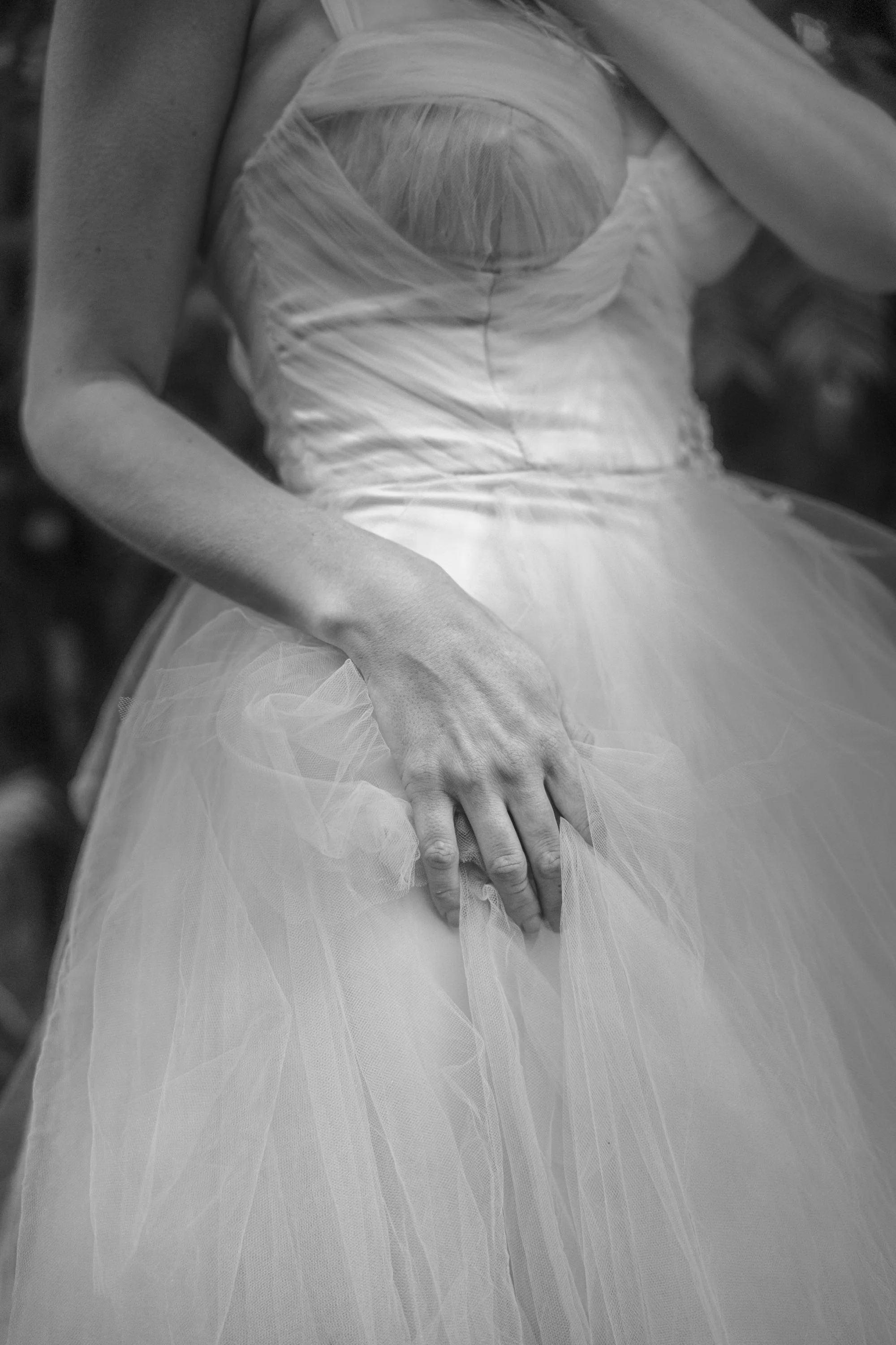 Close-up of a person adjusting a wedding dress, focusing on the hand gently holding the tulle fabric.