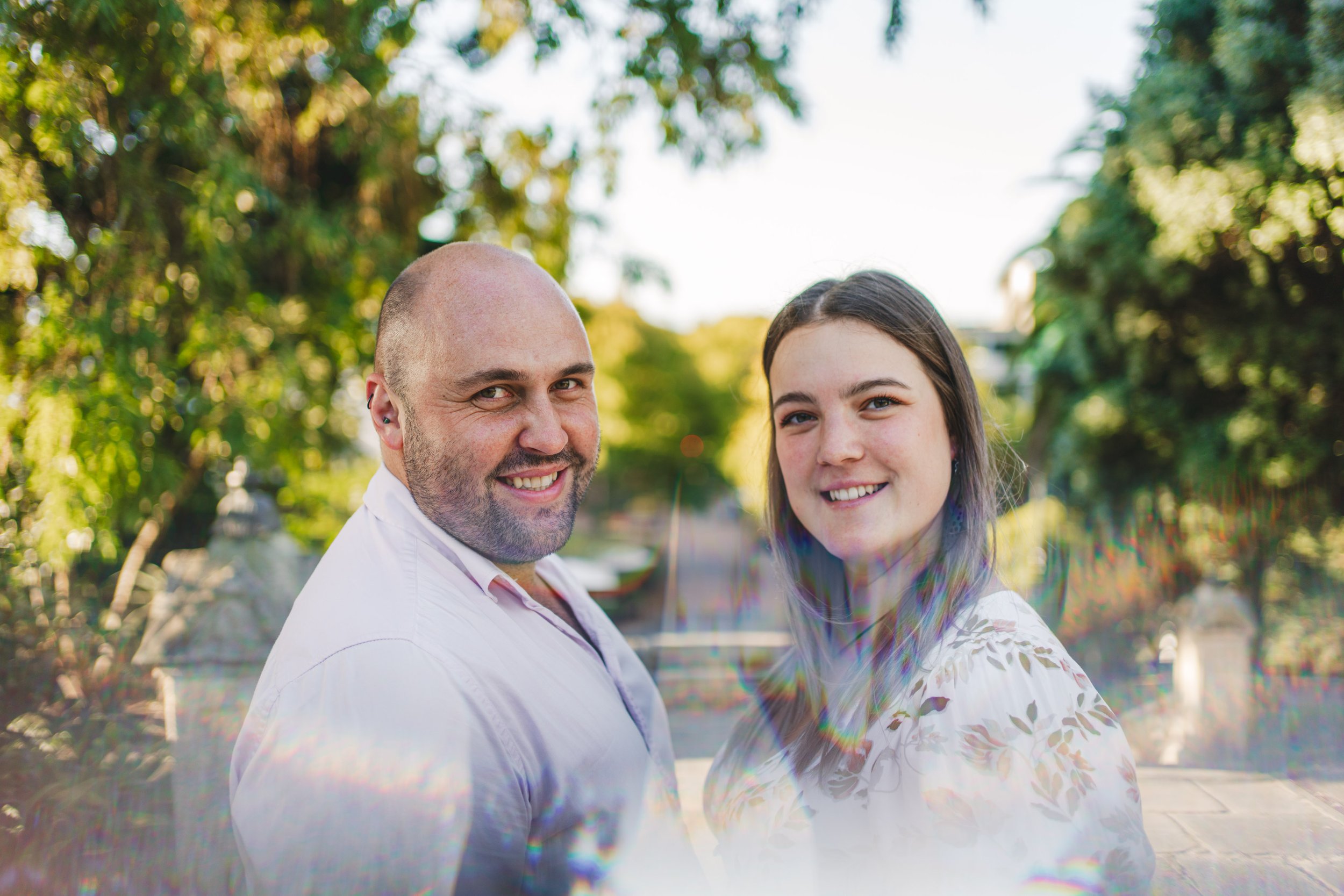 Smiling man and woman outdoors with green trees in the background