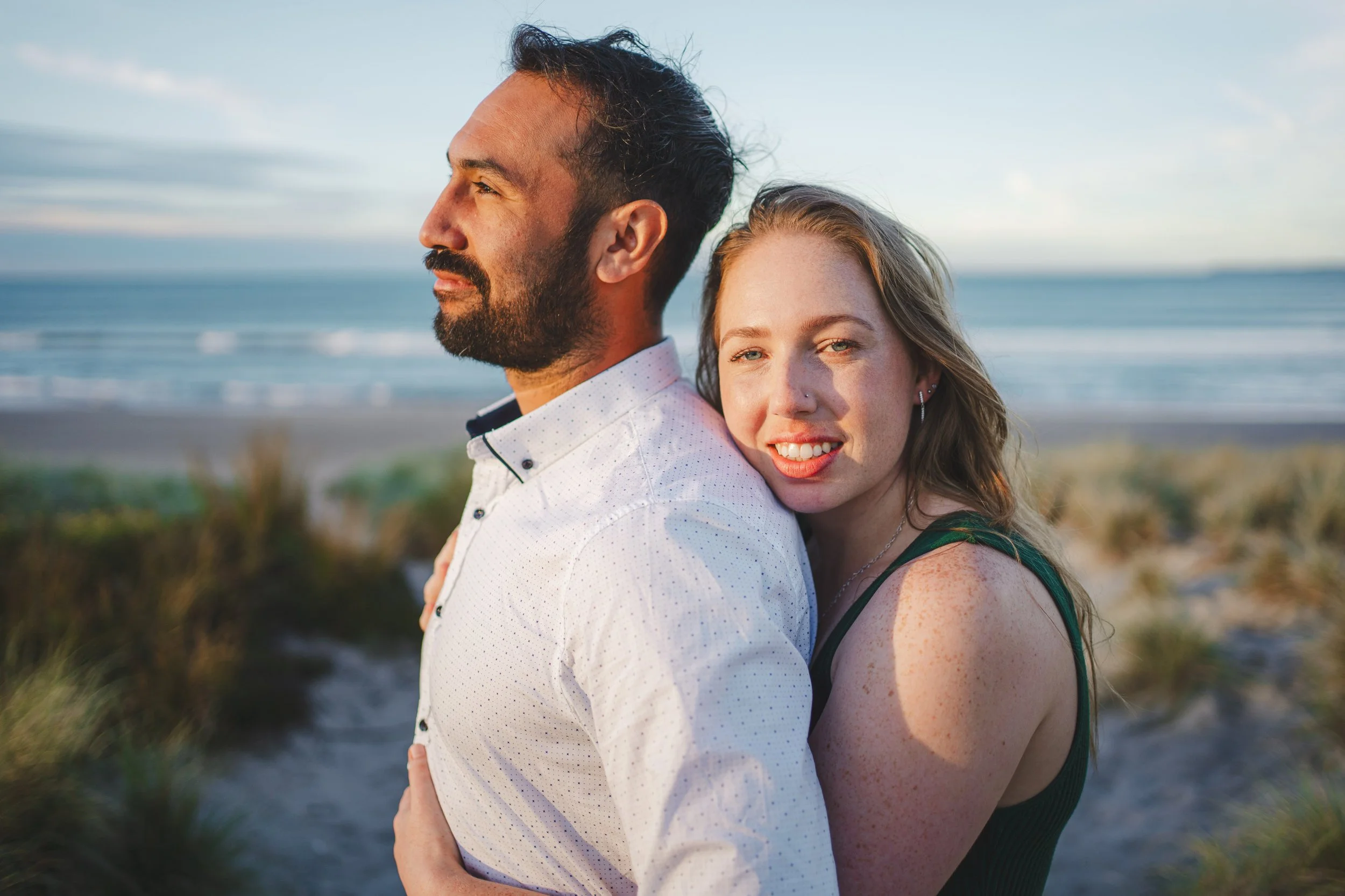 A man and woman embrace on the beach at sunset, with the ocean and sky in the background.