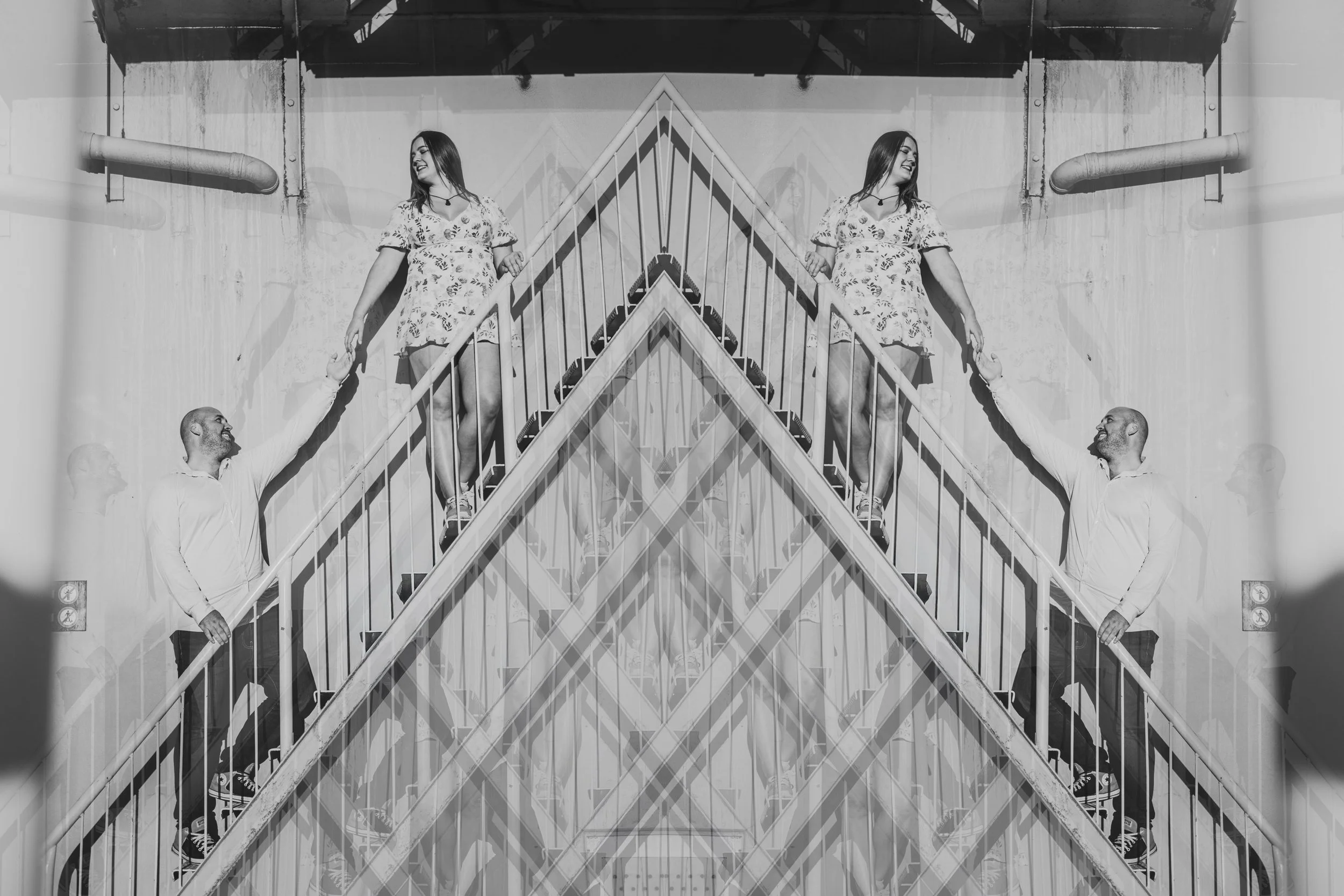 A mirrored black and white photo of a man and woman on a staircase touching hands, with the photo reflecting to create a symmetrical pattern.