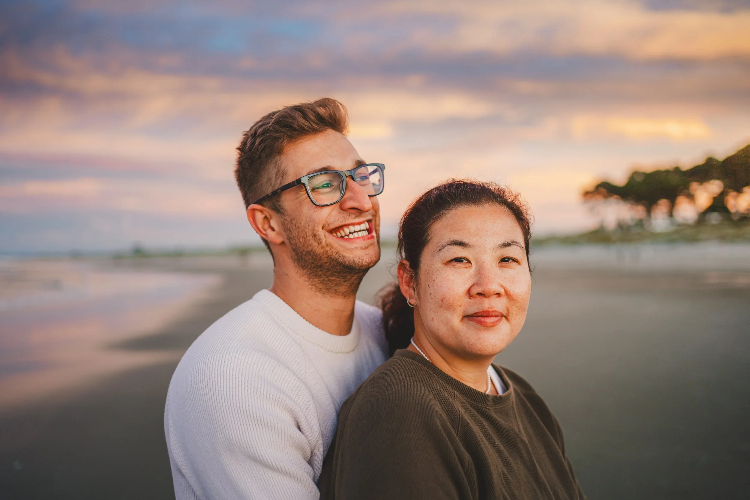 A happy couple standing on the beach at sunset, smiling and enjoying the scenery.
