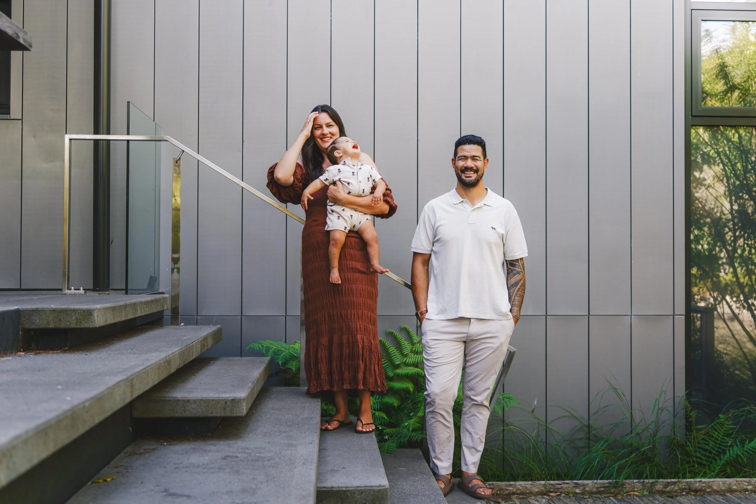 A family of three standing outside a modern building, with the woman holding a toddler and the man standing beside her smiling.