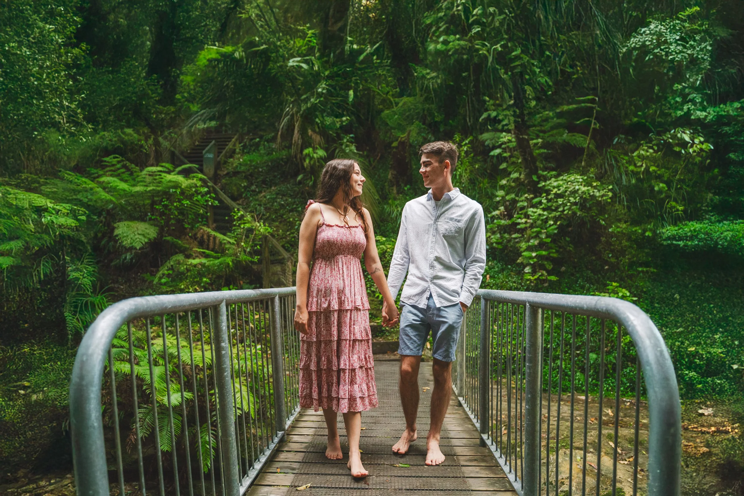 A young couple walking hand-in-hand on a wooden bridge in a lush green forest.