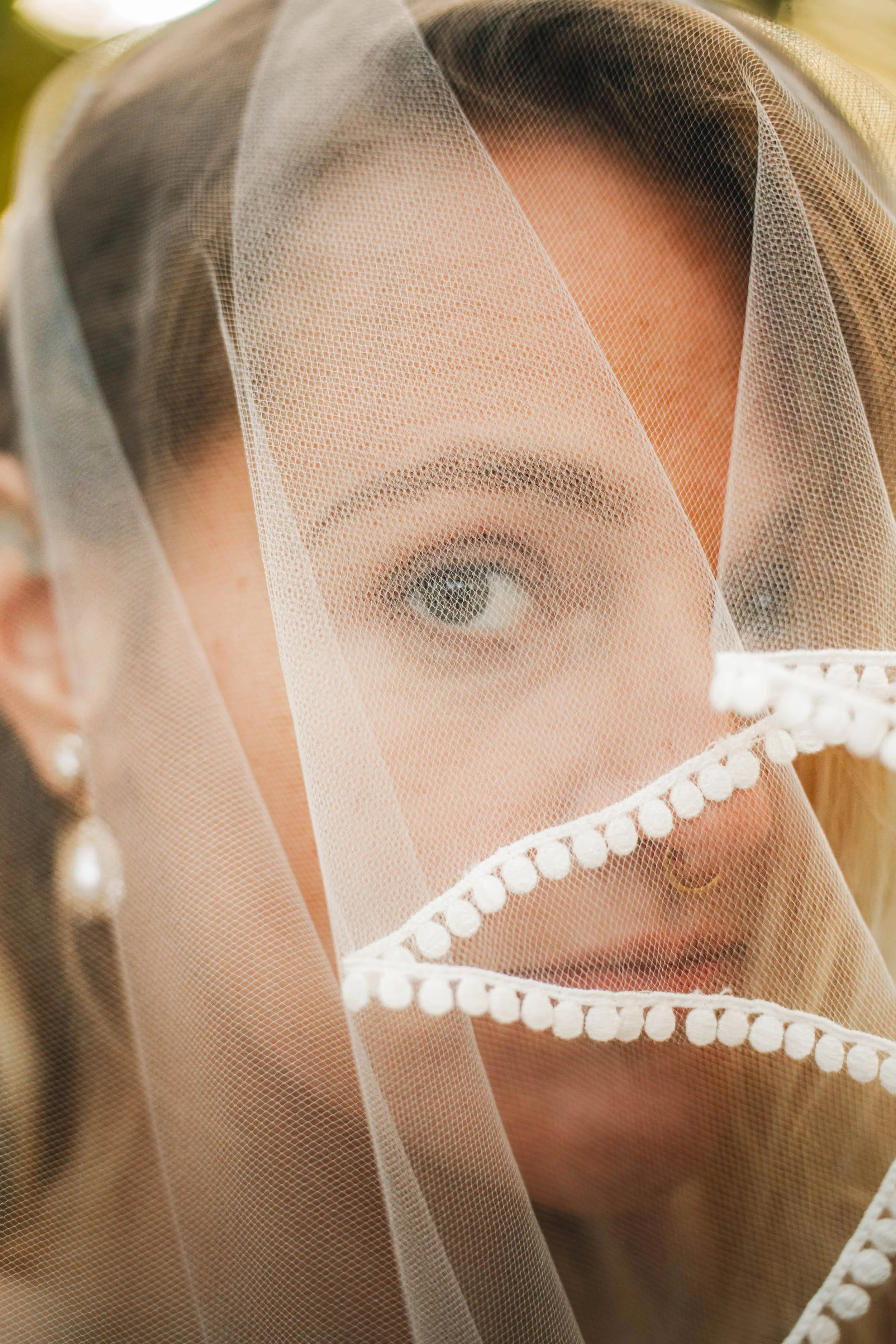 A woman with a veil covering her face, revealing only her eye and part of her face, wearing earrings and a nose ring.