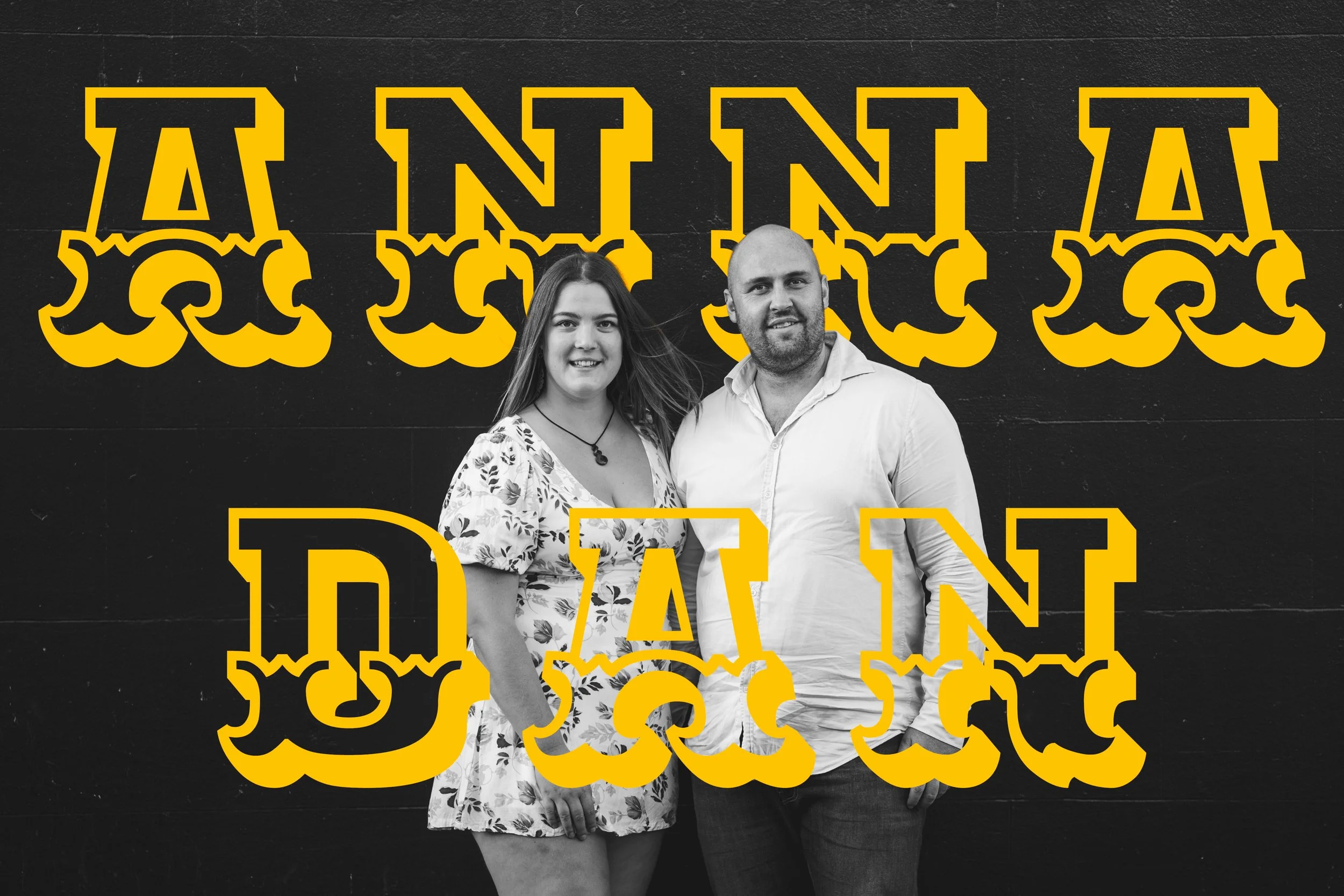 A black and white photo of a woman and a man standing in front of a black wall, with the words "ANNA" and "DAN" in large yellow and black outlined letters