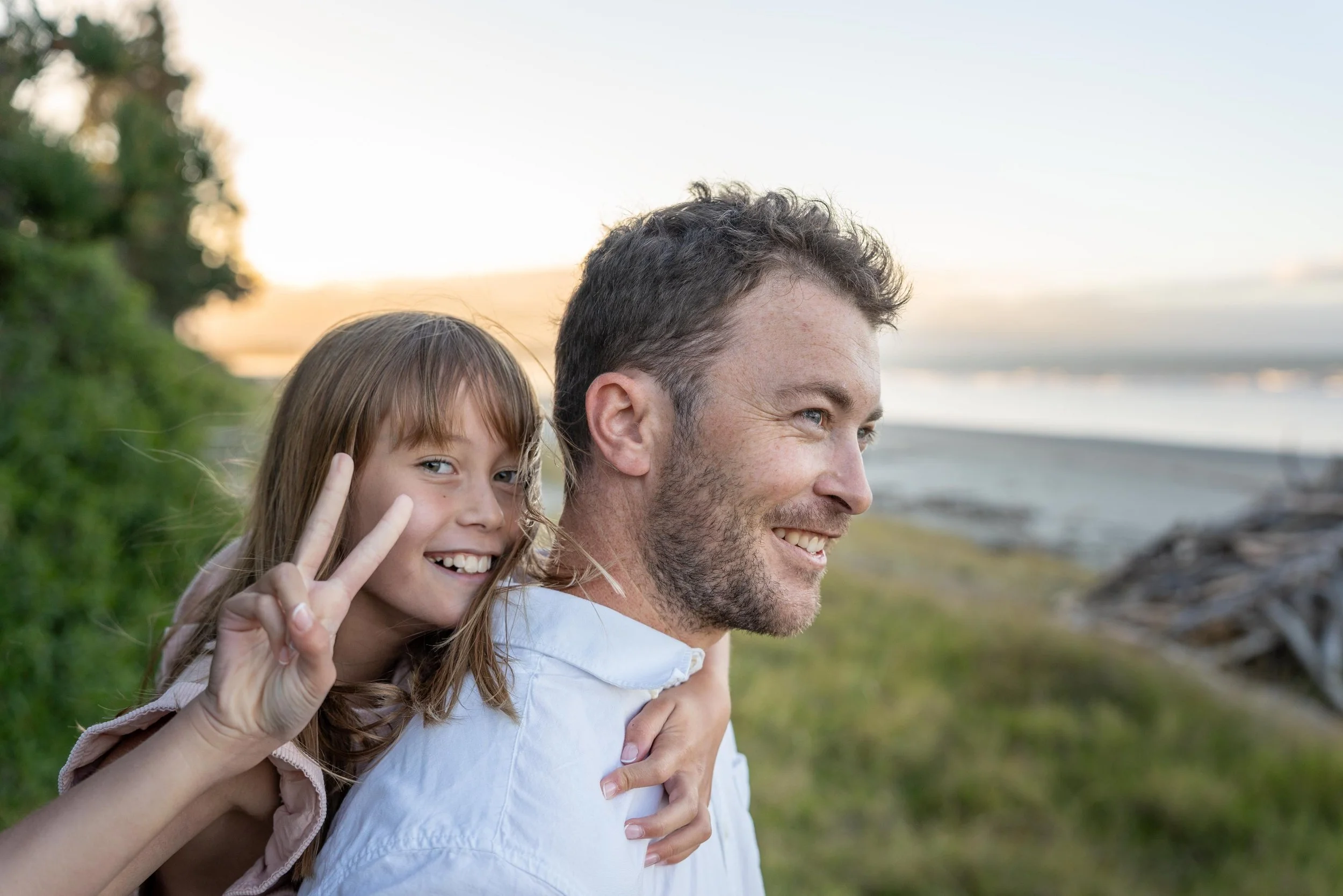 A young girl giving a piggyback ride on a man's back at the beach during sunset.