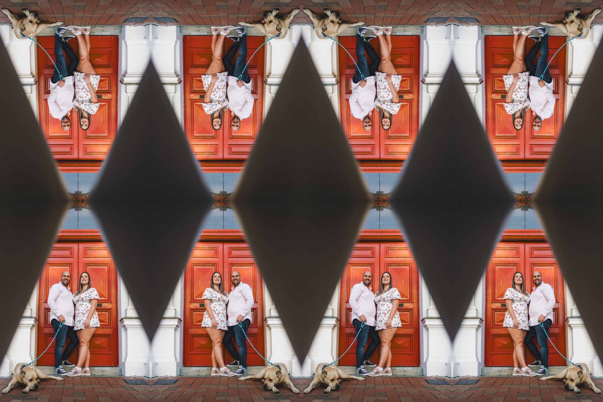 A man and woman standing together with a dog on a leash in front of a red door, with a mirrored reflection above showing the same scene, divided by black diamond-shaped patterns.
