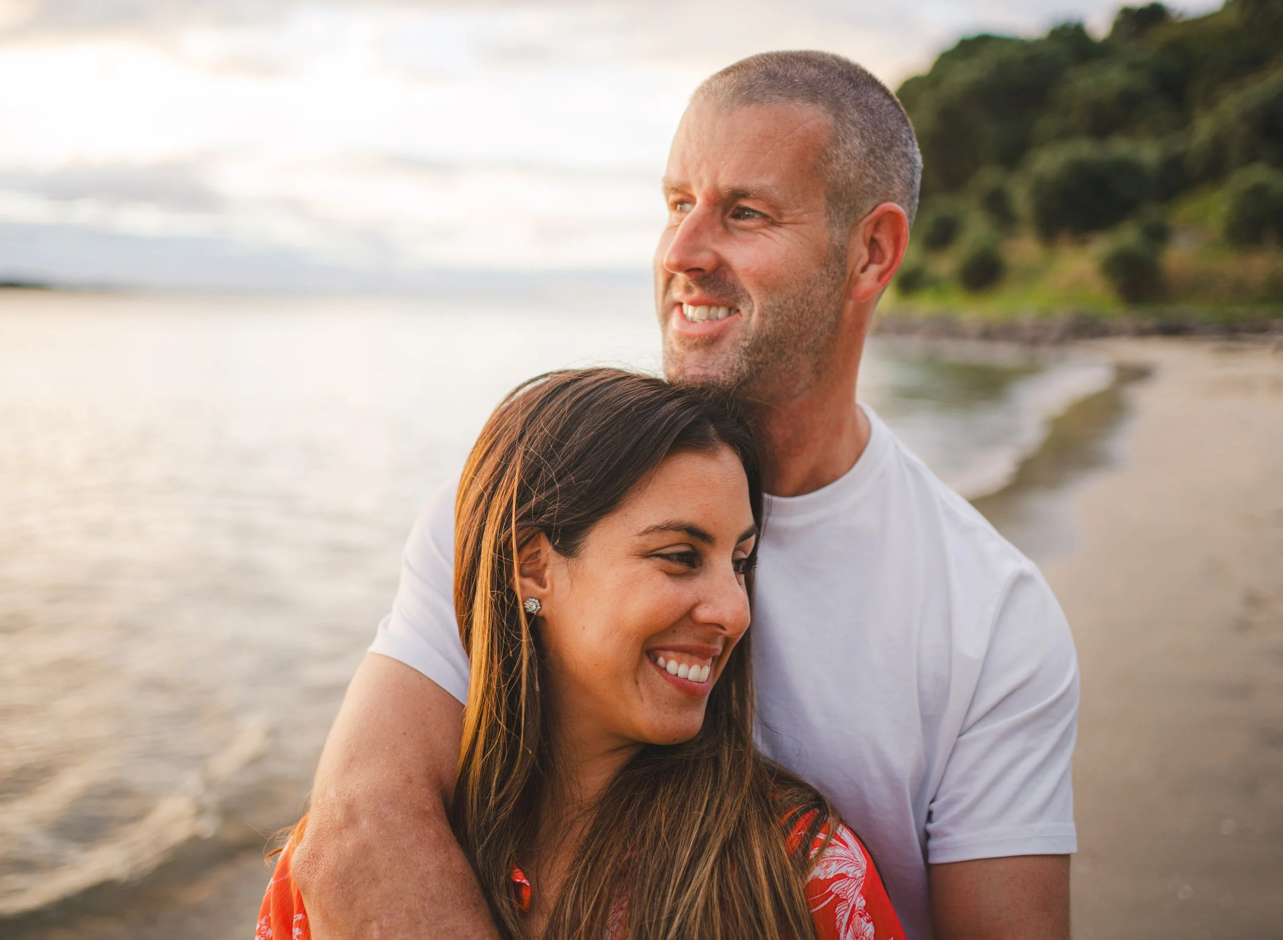 A smiling man and woman hugging on a beach at sunset