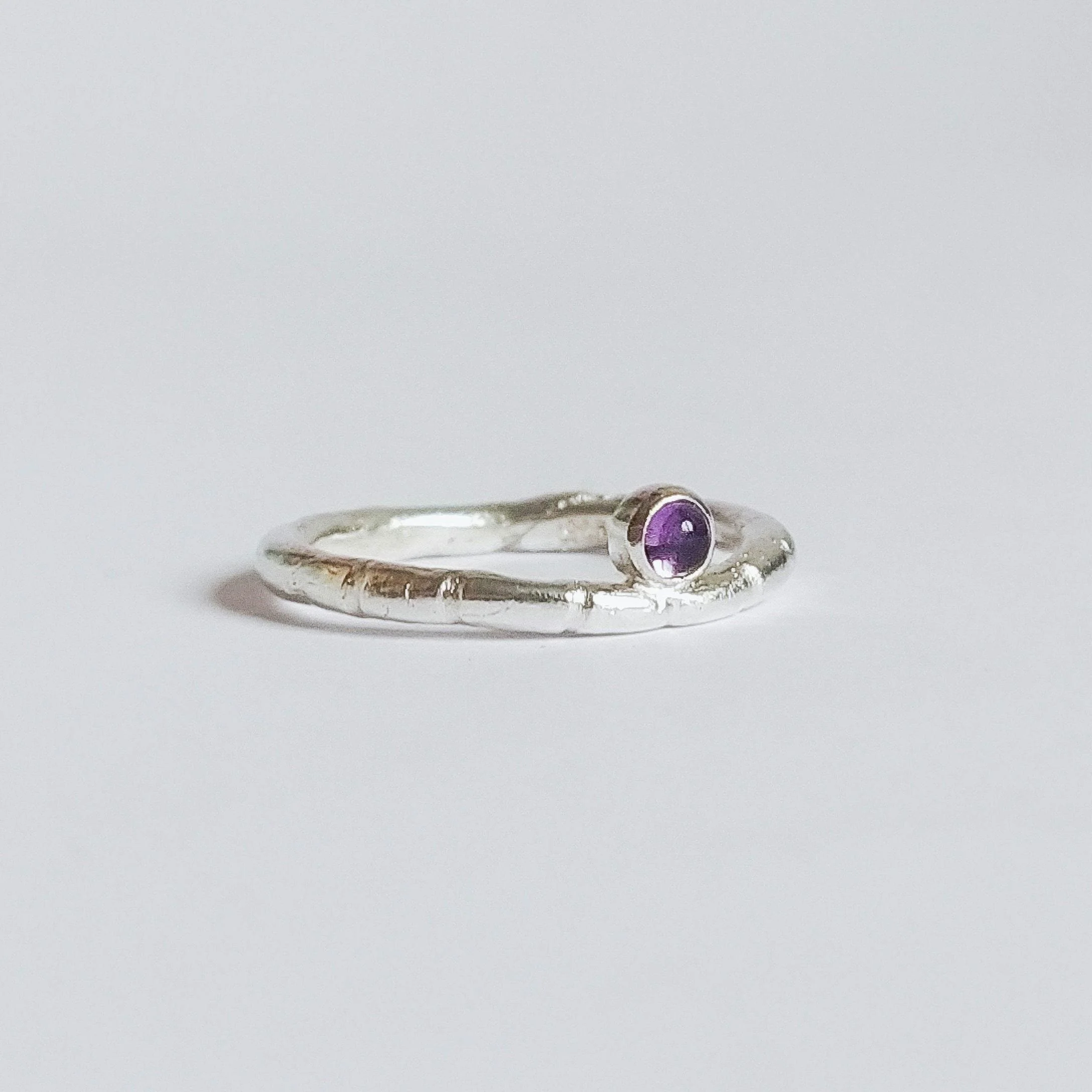 Close-up image of a silver ring with a purple gemstone on a plain white background.