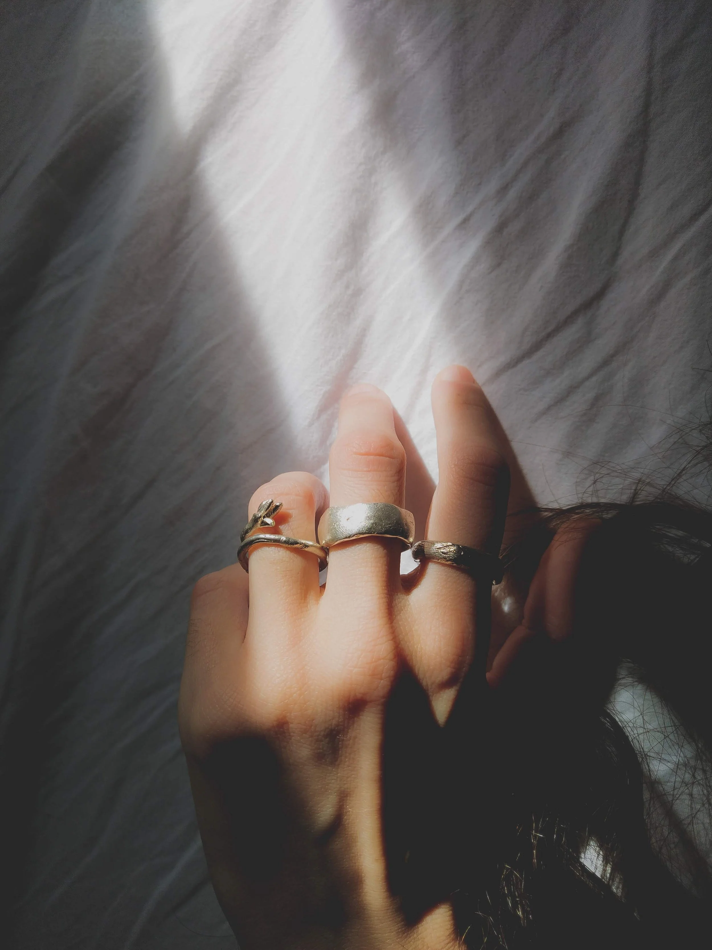 Close-up of a person's hand with several silver rings, resting on a soft surface with sunlight shining on the hand.