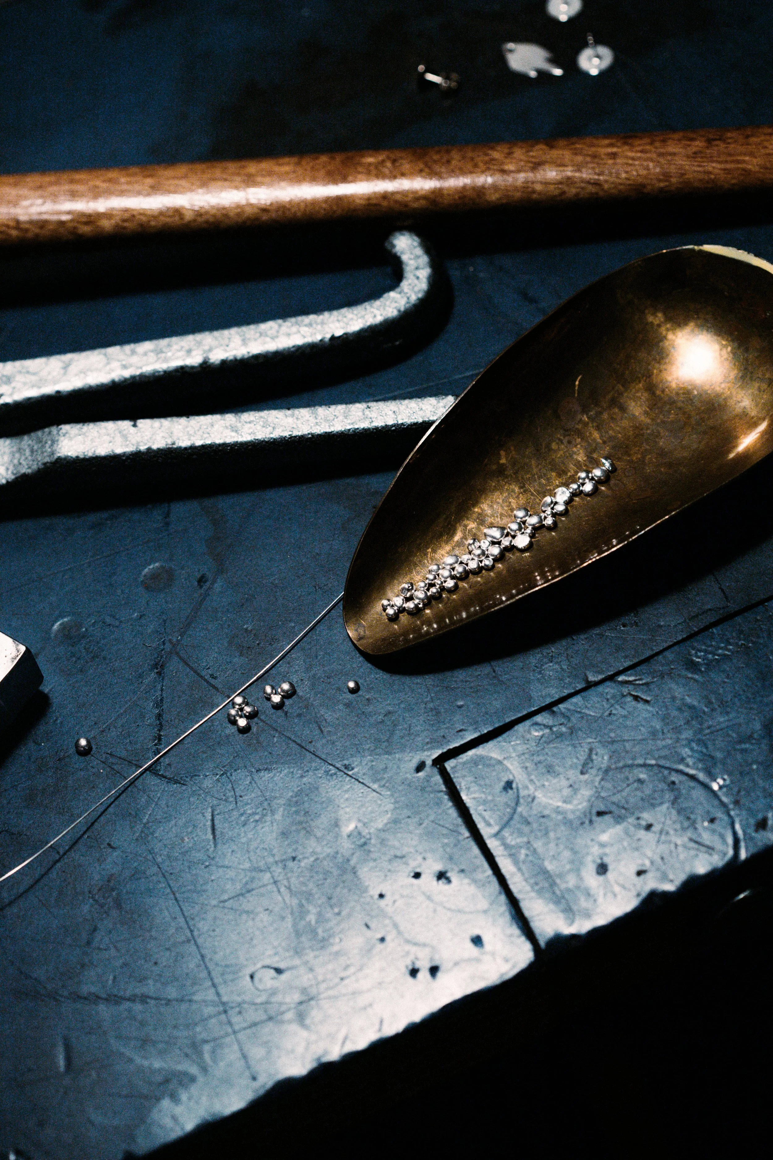 Close-up of a metallic gold scoop with small silver balls inside, a large metal hook, and various small metallic objects on a dark surface.