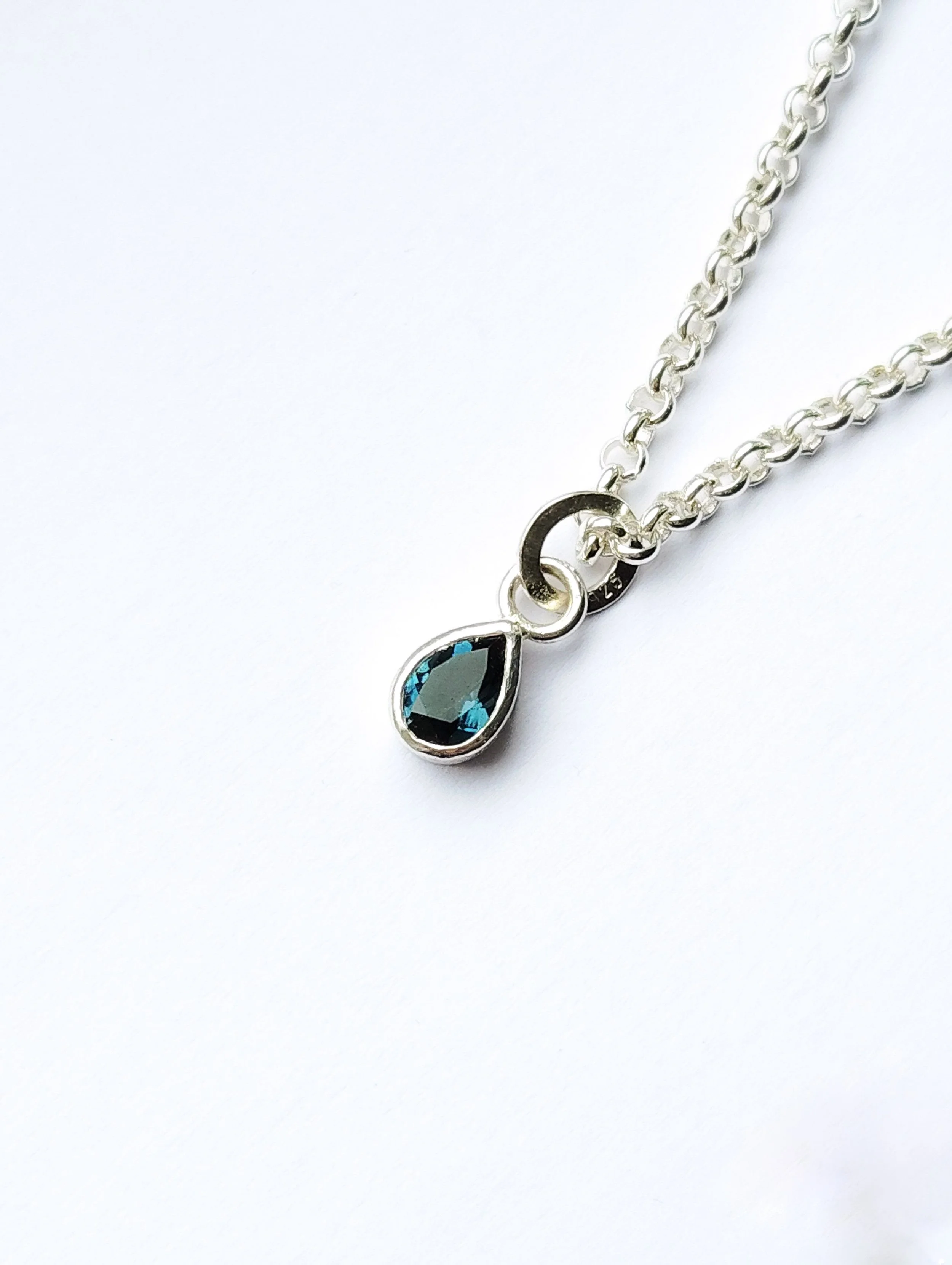 A silver chain necklace with a teardrop-shaped gemstone pendant, lying on a white surface.