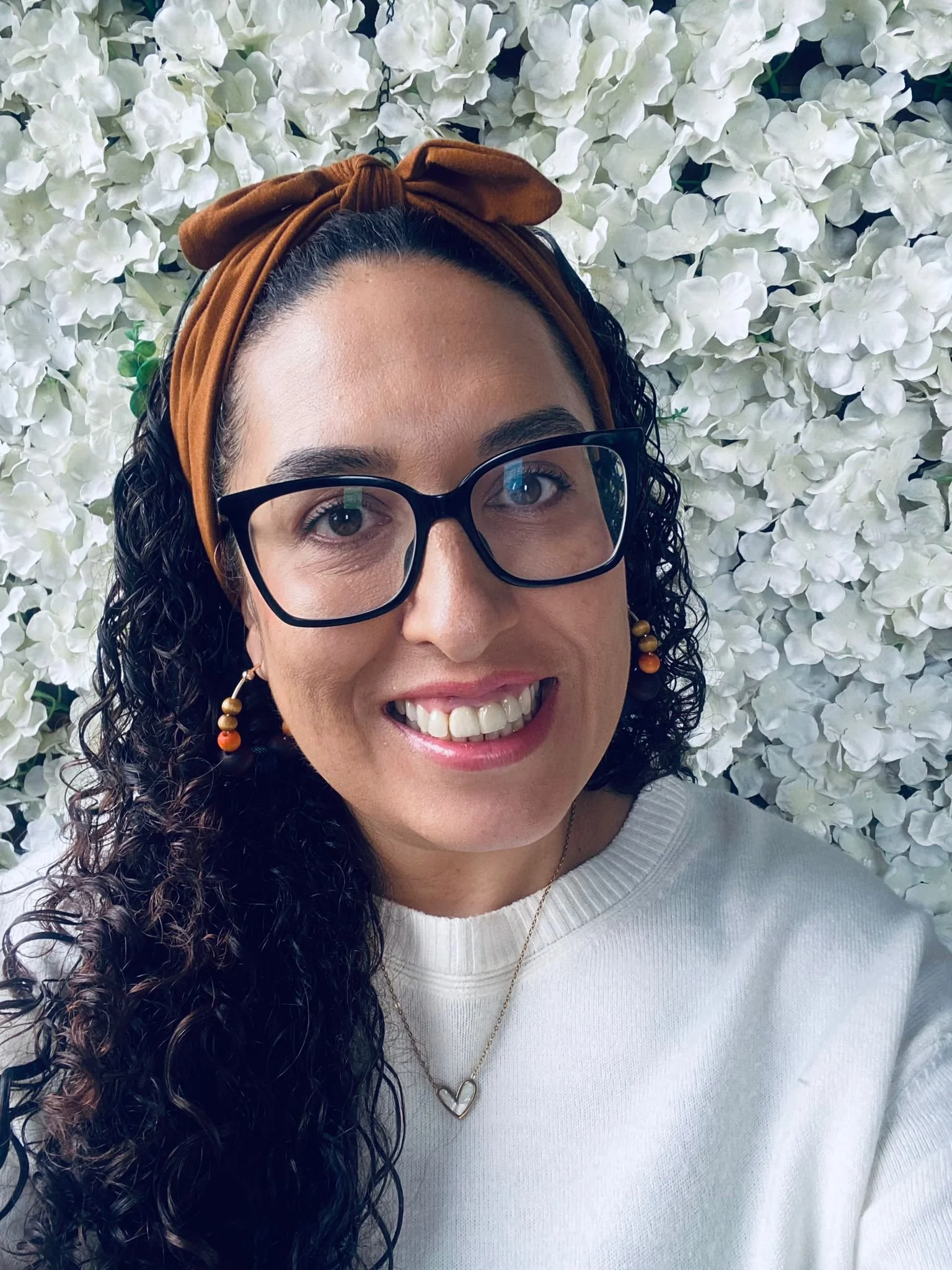 A woman receiving a gentle massage on her forehead from another person, lying on a black pillow with a geometric design, near a large window with a view of trees outside.