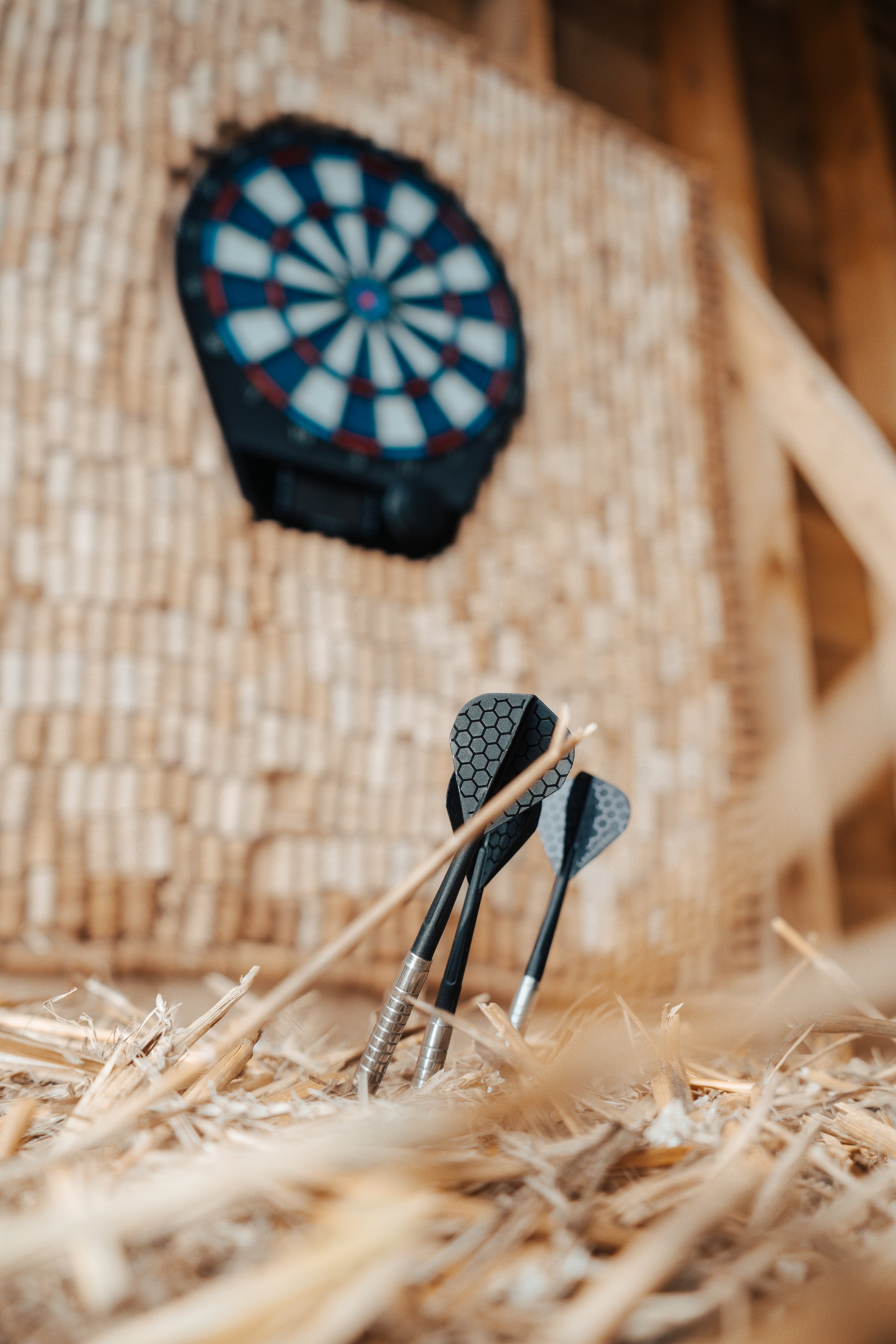 Des fléchettes plantées dans du bois, avec un tableau de jeu de fléchettes en arrière-plan.