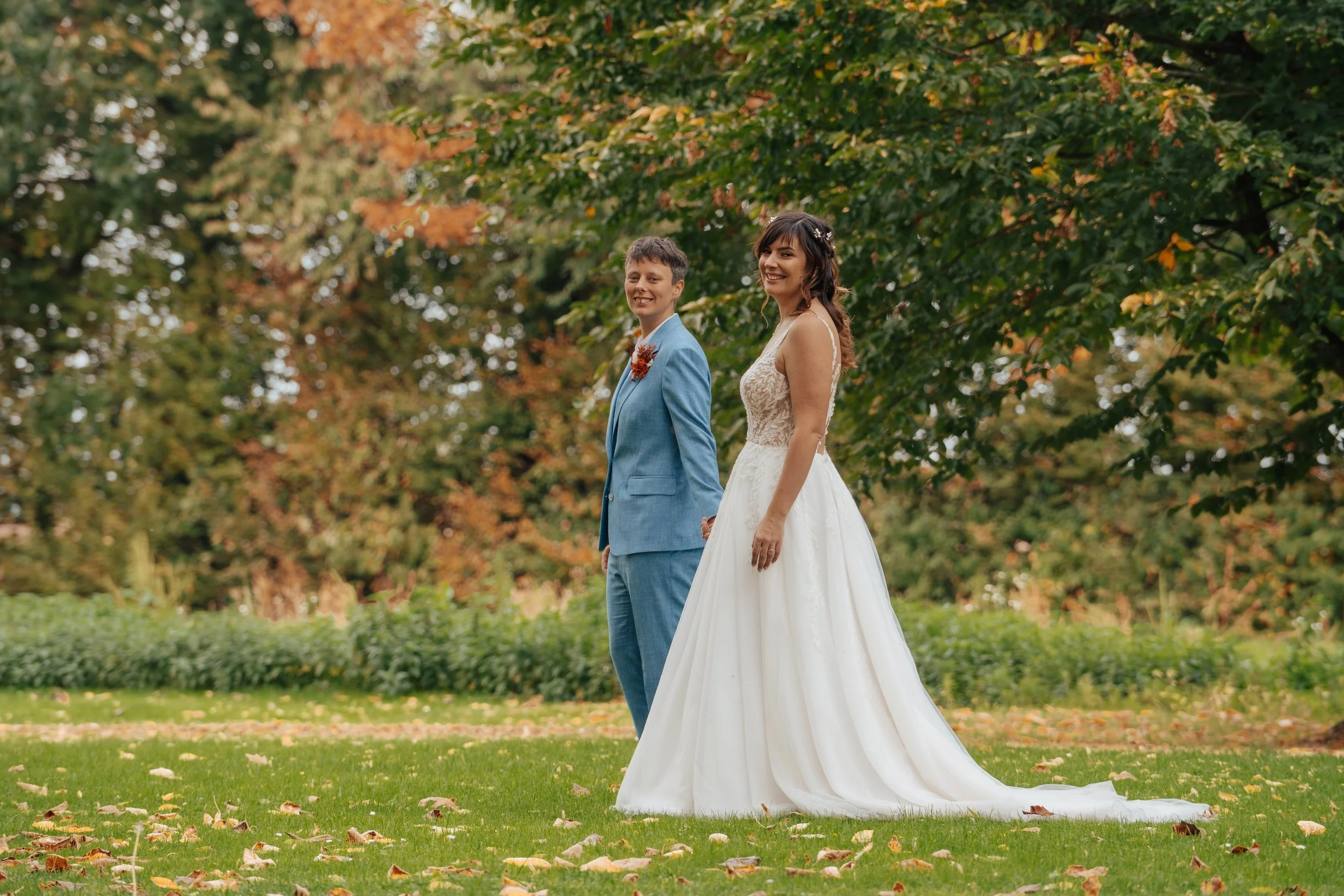 Un couple en tenue de mariage dans un parc en automne, souriant, entouré d'arbres aux feuilles multicolores.