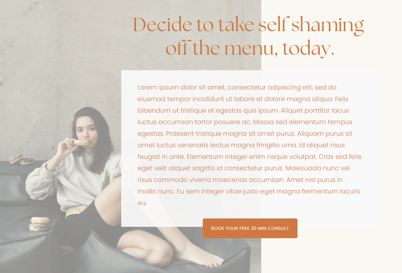 A woman sitting on a black couch, eating a donut, with other donuts placed on a table behind her. She has shoulder-length dark hair and is wearing a light-colored hoodie and black shorts.