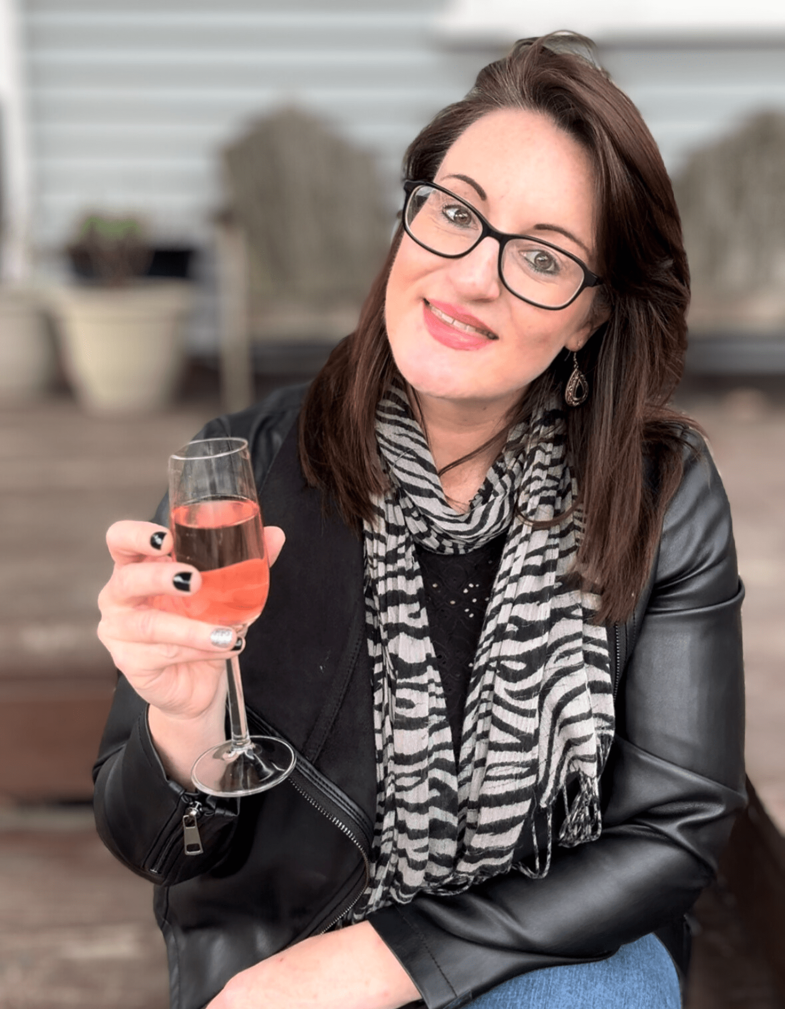 Squarespace web designer wearing black-rimmed glasses, black leather jacket and stripy scarf who is holding up a glass of Rose sparkling wine in celebration.