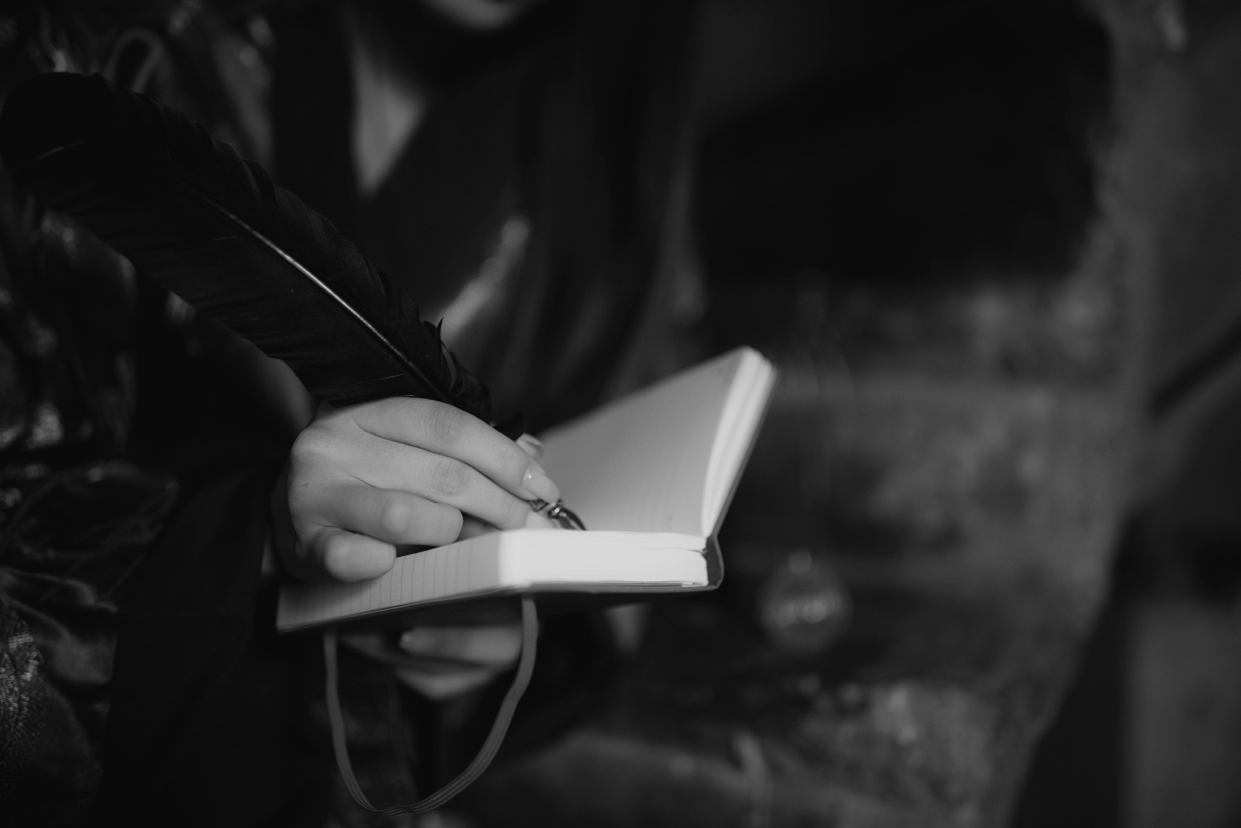 Close-up of a person's hand writing in a small notebook with a pen, black and white indoor setting.