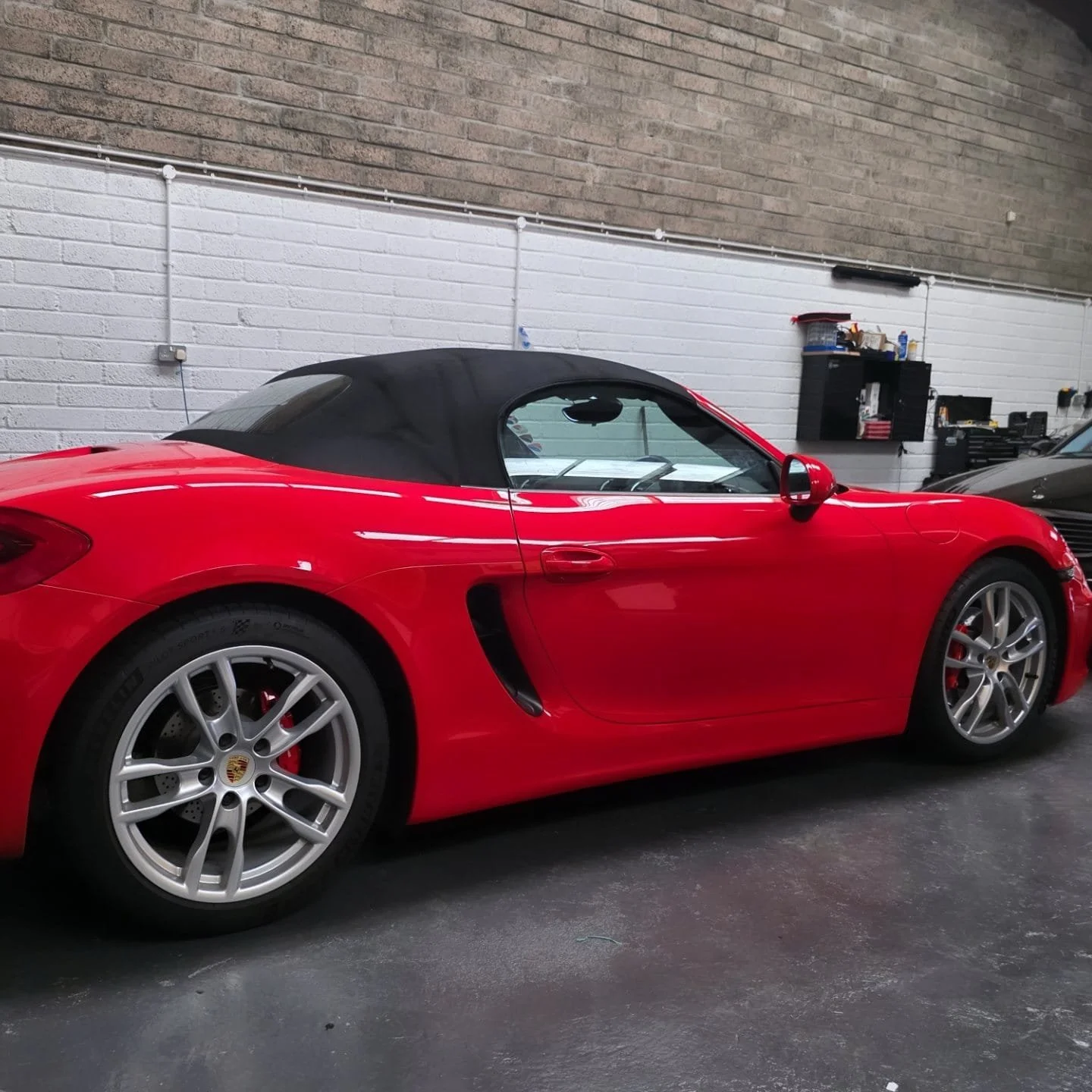 Red Porsche convertible with black soft top parked inside a garage.