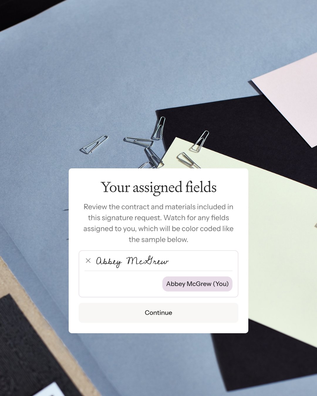 A digital interface displaying a section titled 'Your assigned fields' with a name 'Abby McAndrew' marked as assigned to the user, over a background of layered colored papers and scattered paper clips.