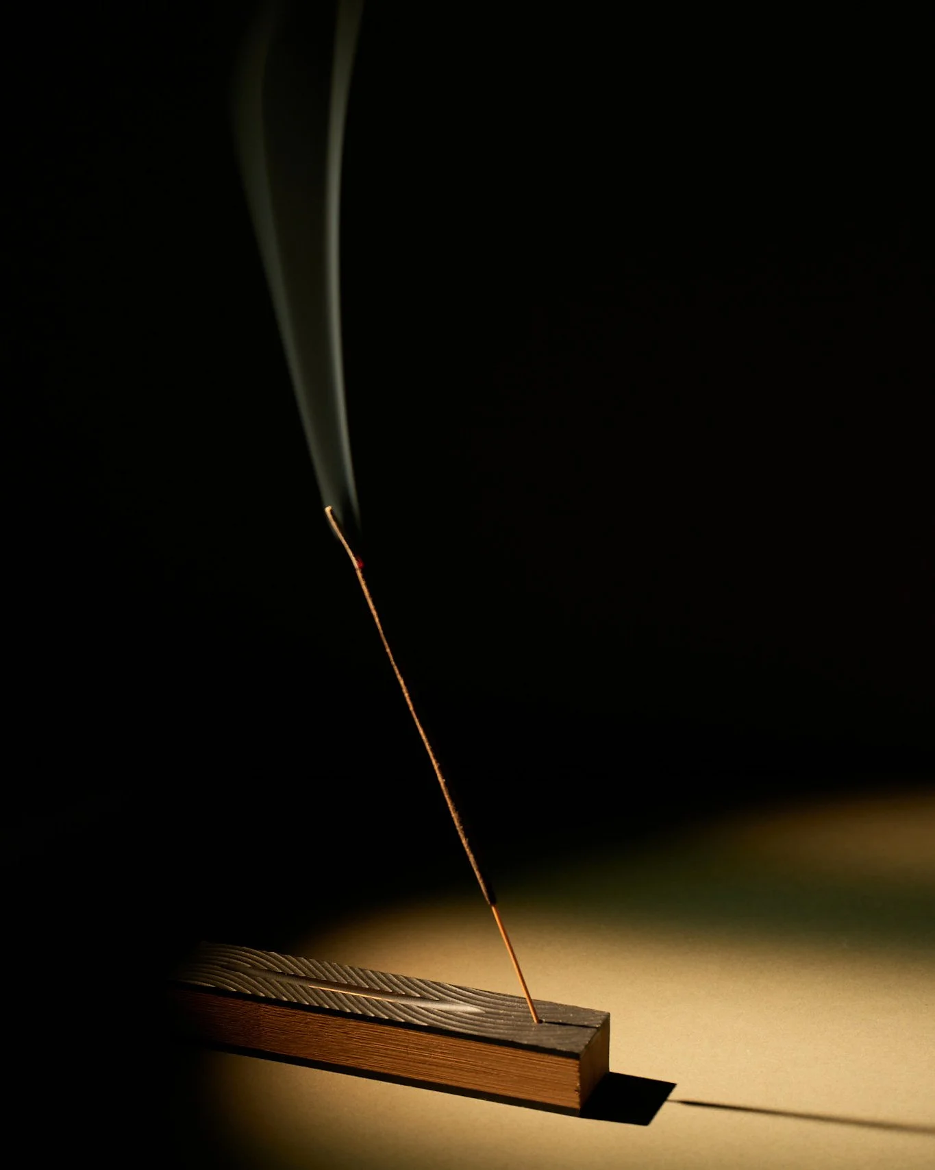 A lit incense stick emitting smoke, placed in a bamboo holder on a japanese garden surface, with a dark background.