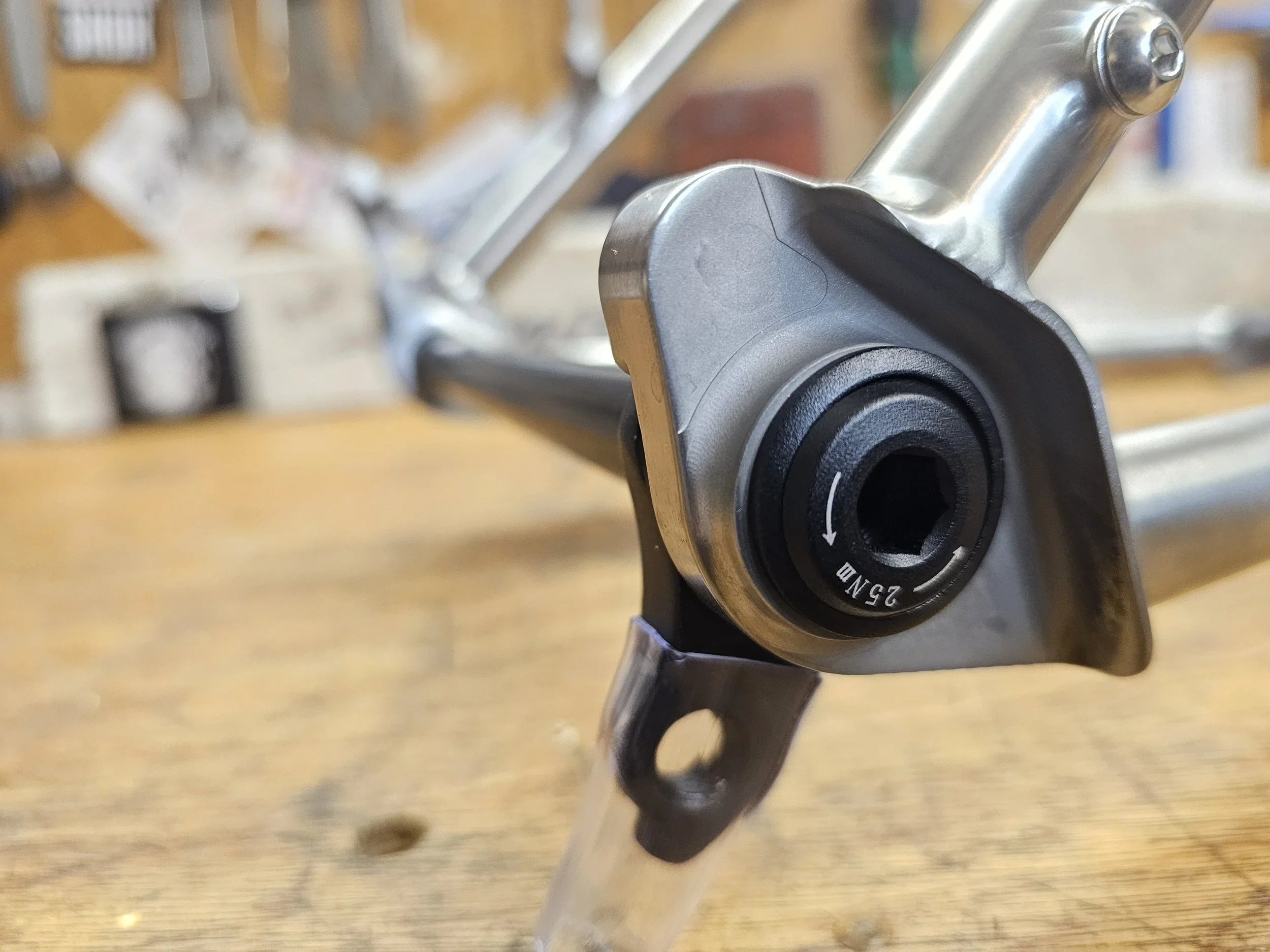 Close-up of a UDH Gear hanger attached to a Smokestone Bikes titanium frame, on a wooden bench