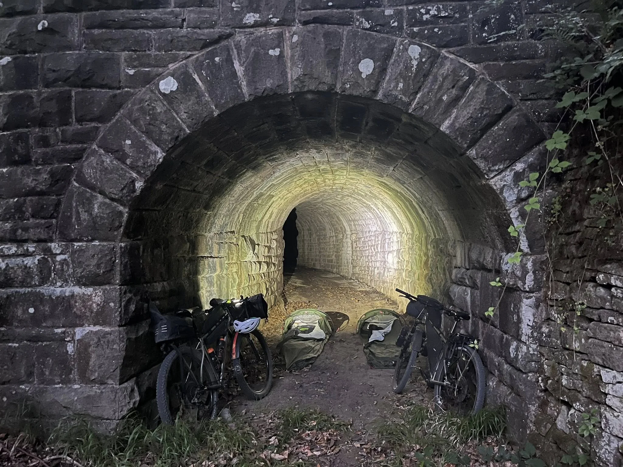 Two bicycles and camping gear inside a stone tunnel at dusk.