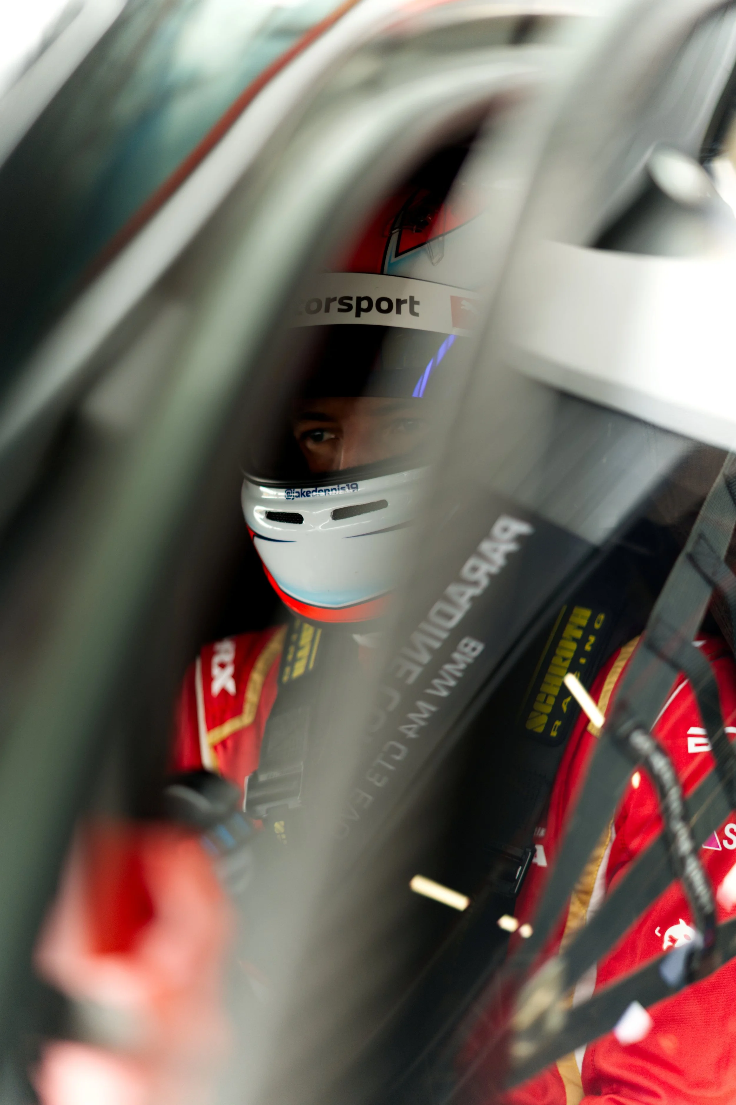 A race car driver with a helmet, seated inside a race car, looking through the window.