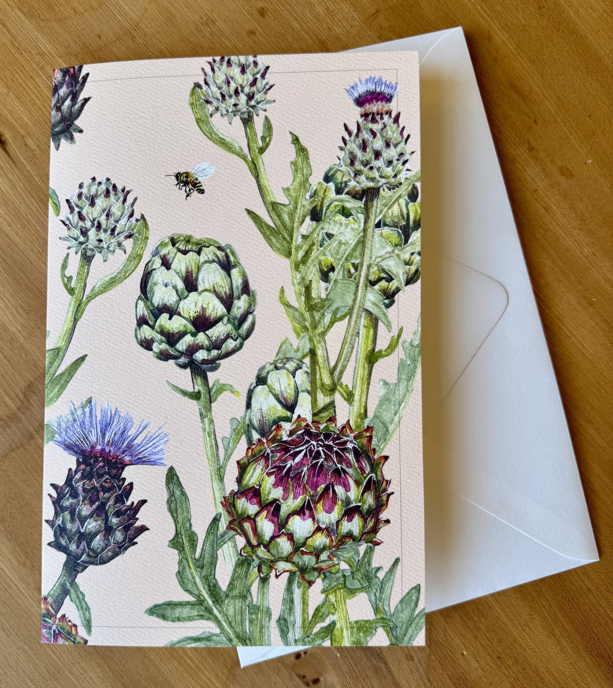 Illustration of multiple artichokes and a bee on one of the artichokes, on textured white paper.