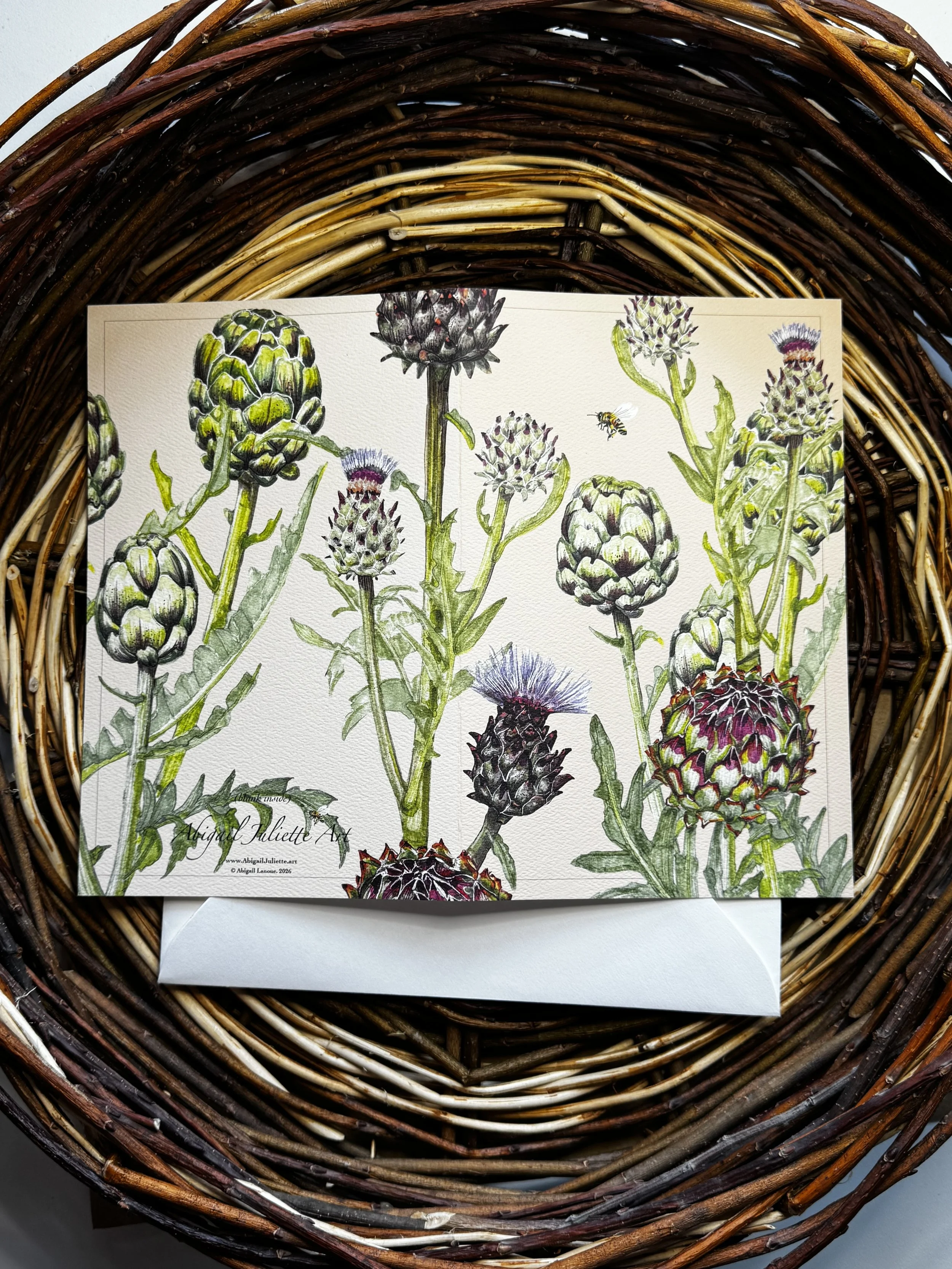 Close-up view of a botanical illustration of artichokes, with detailed green and purple flowering plants, set on a piece of paper in a woven wicker basket.