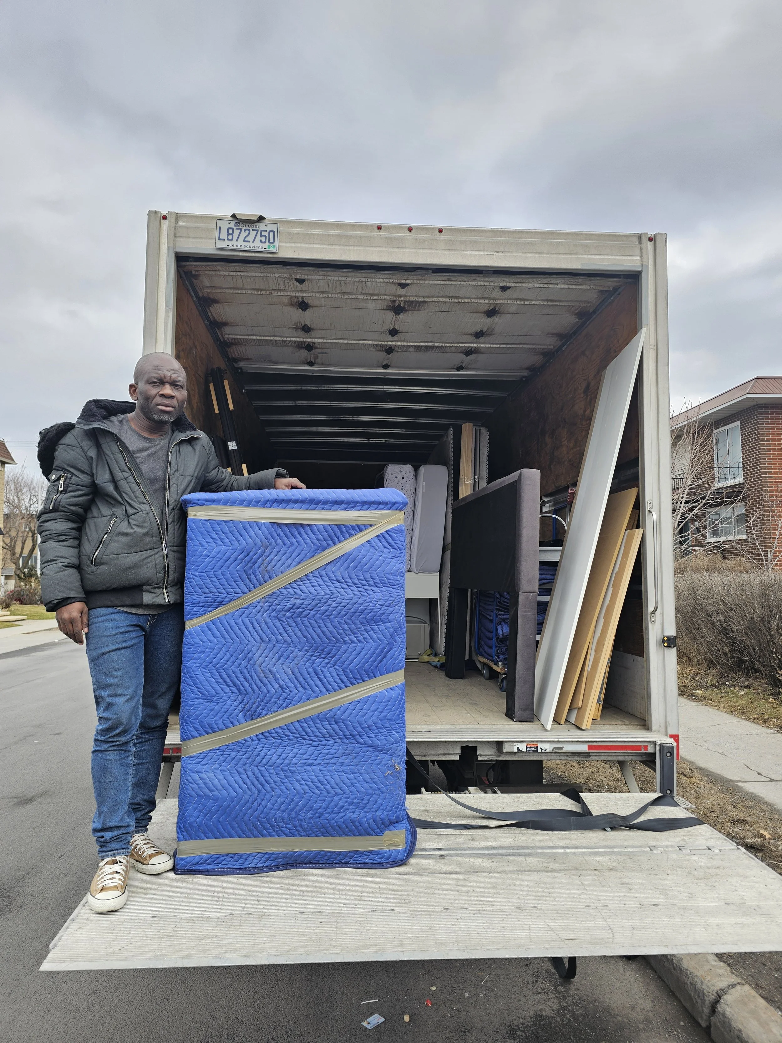 Un homme se tient à côté d'un camion de déménagement ouvert, contenant des meubles protégés par des couvertures bleues.