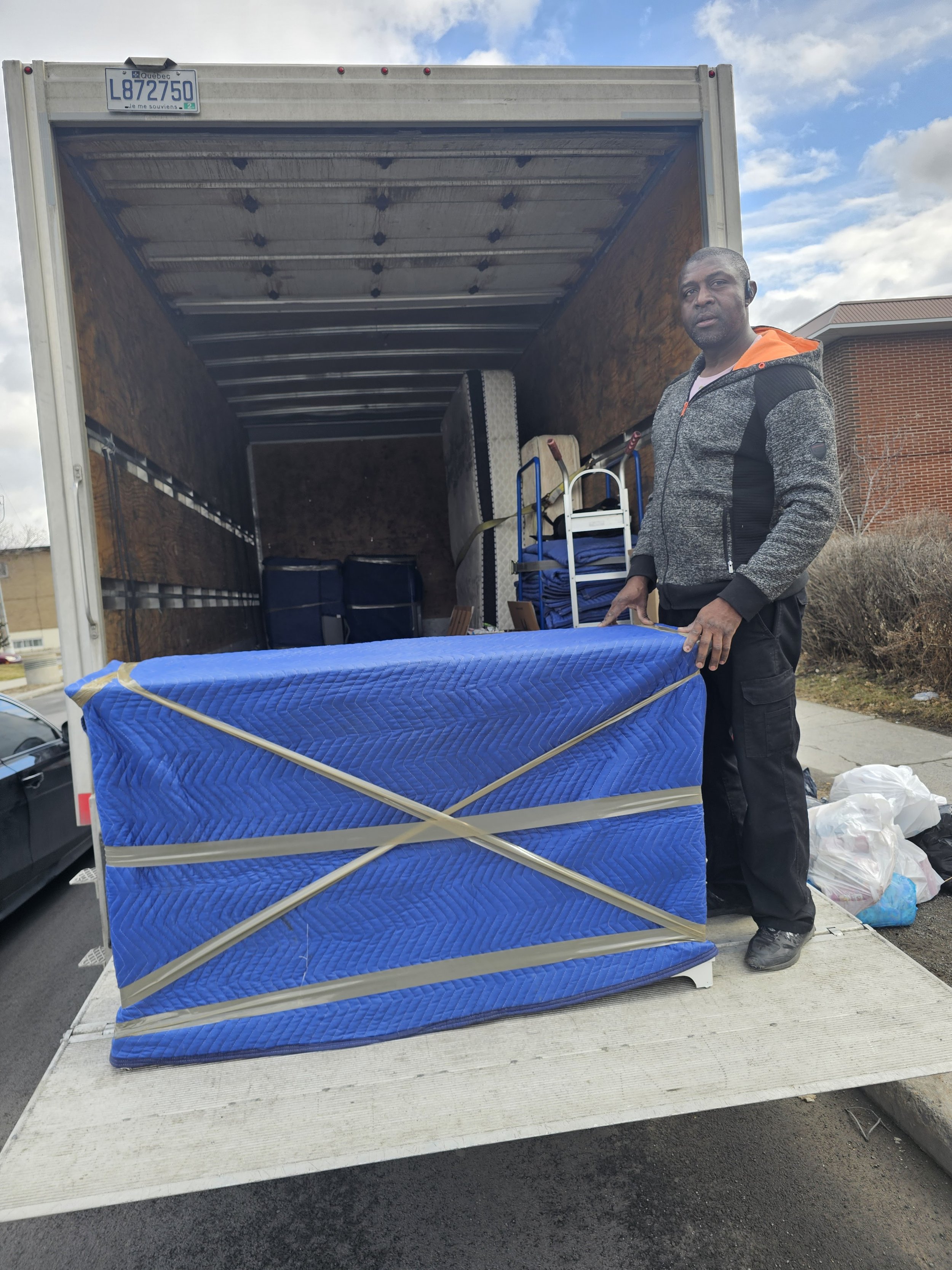 Déménagement avec un camion, un homme et des objets emballés dans une couverture bleue.