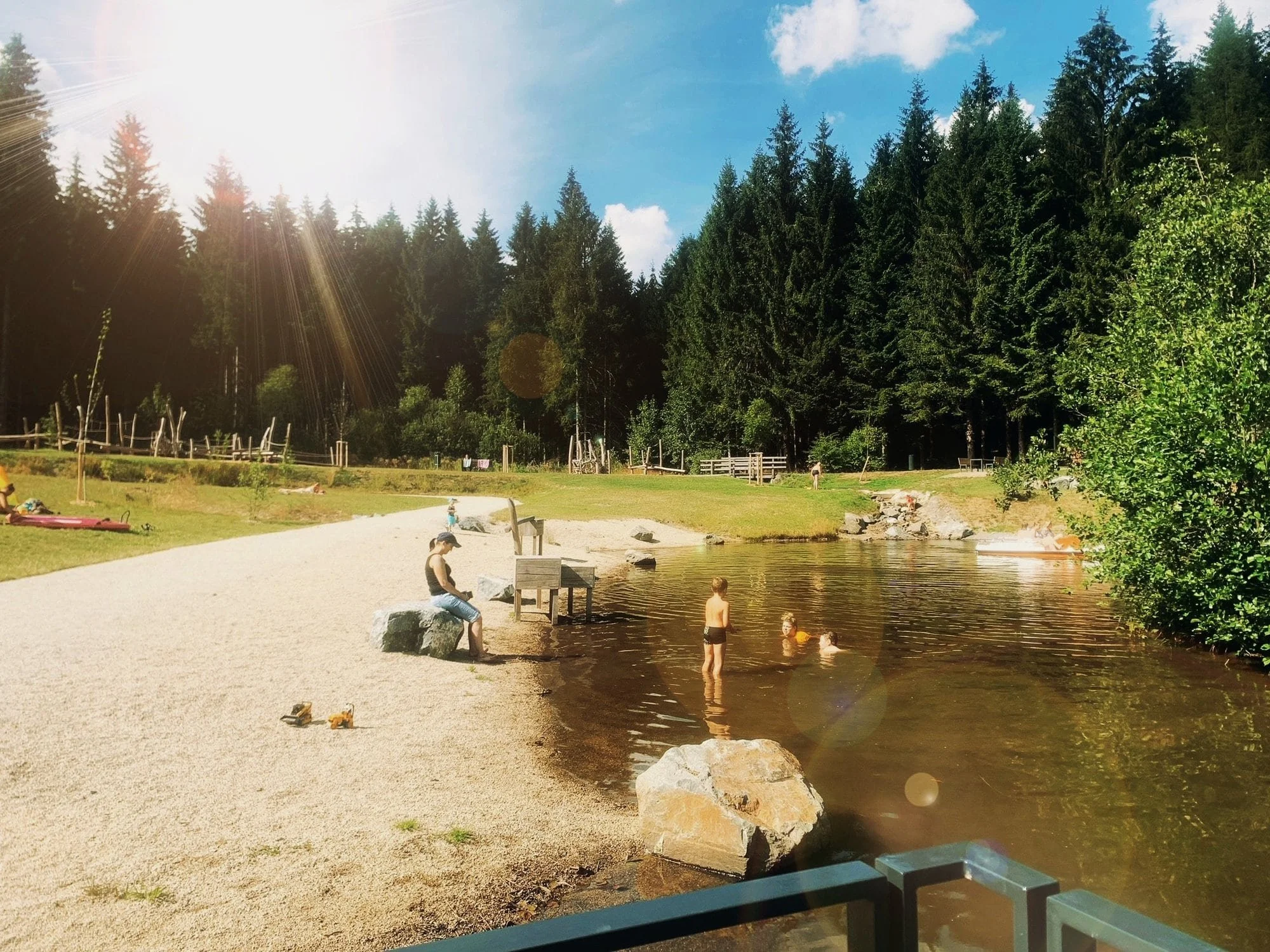 Menschen, die an einem Badeteich im Freien inmitten eines Waldes sitzen, schwimmen und entspannen bei sonnigem Wetter.