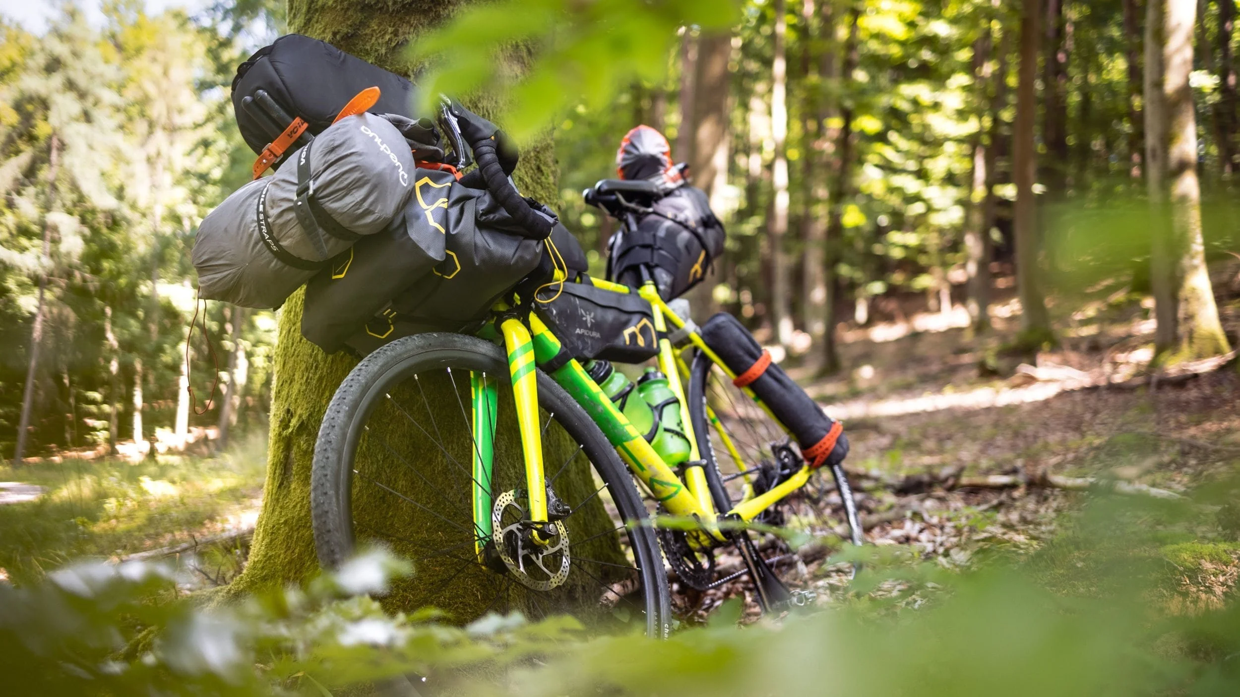 Ein gelbes Mountainbike mit Gepäck und Ausrüstung, das im Wald an einem Baum lehnt.