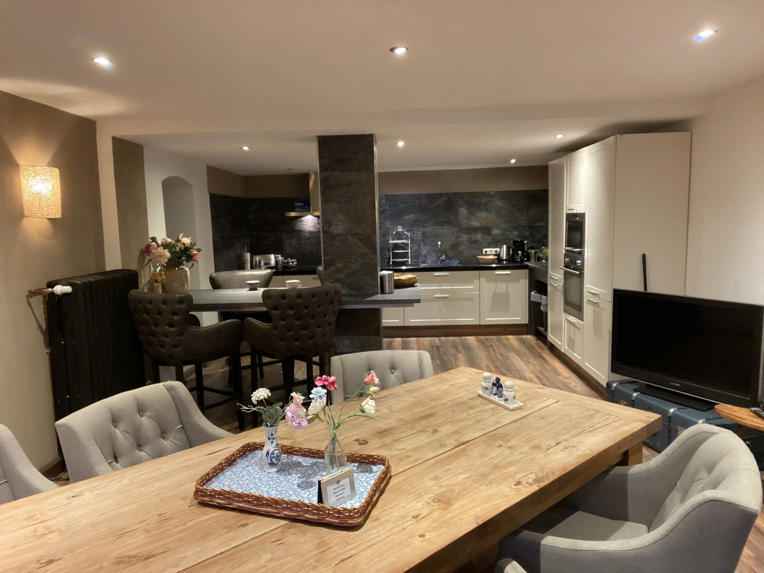 Offene Küche und Essbereich in einem gemütlichen Heim mit dunklen und hellen Möbeln, Blumen auf dem Tisch, Fernseher und moderne Küchengeräte.