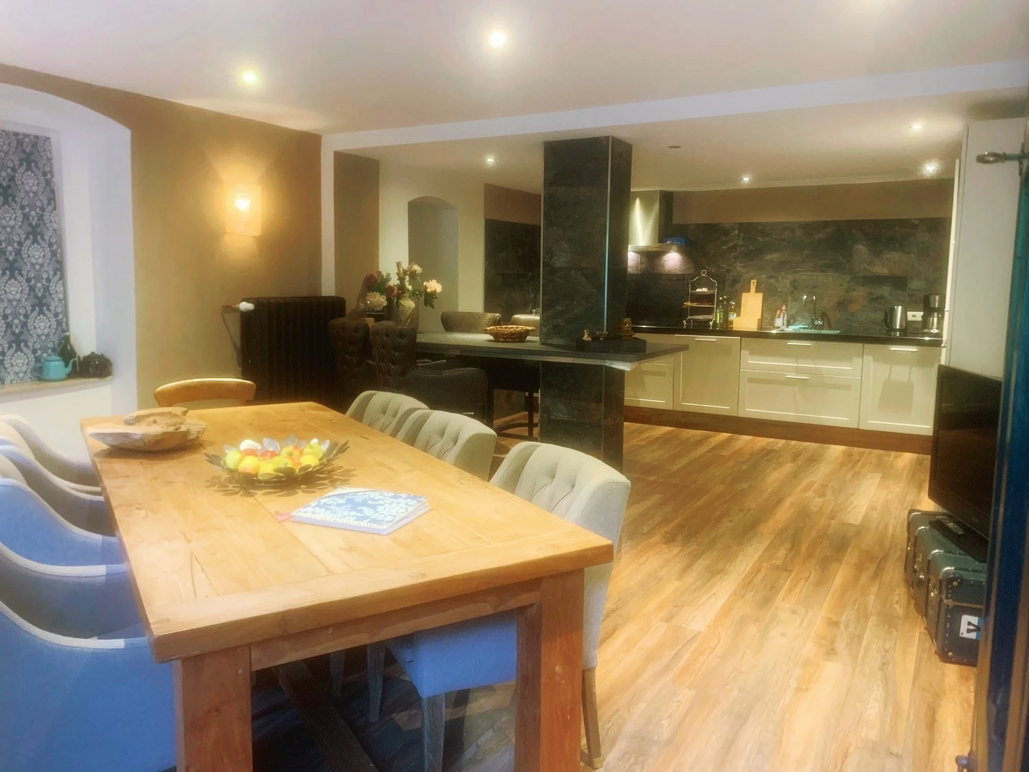 Offene Küche und ein Esszimmertisch in einem modernen Zuhause, mit Holzboden, schwarzen Fliesen, und stilvoller Beleuchtung.