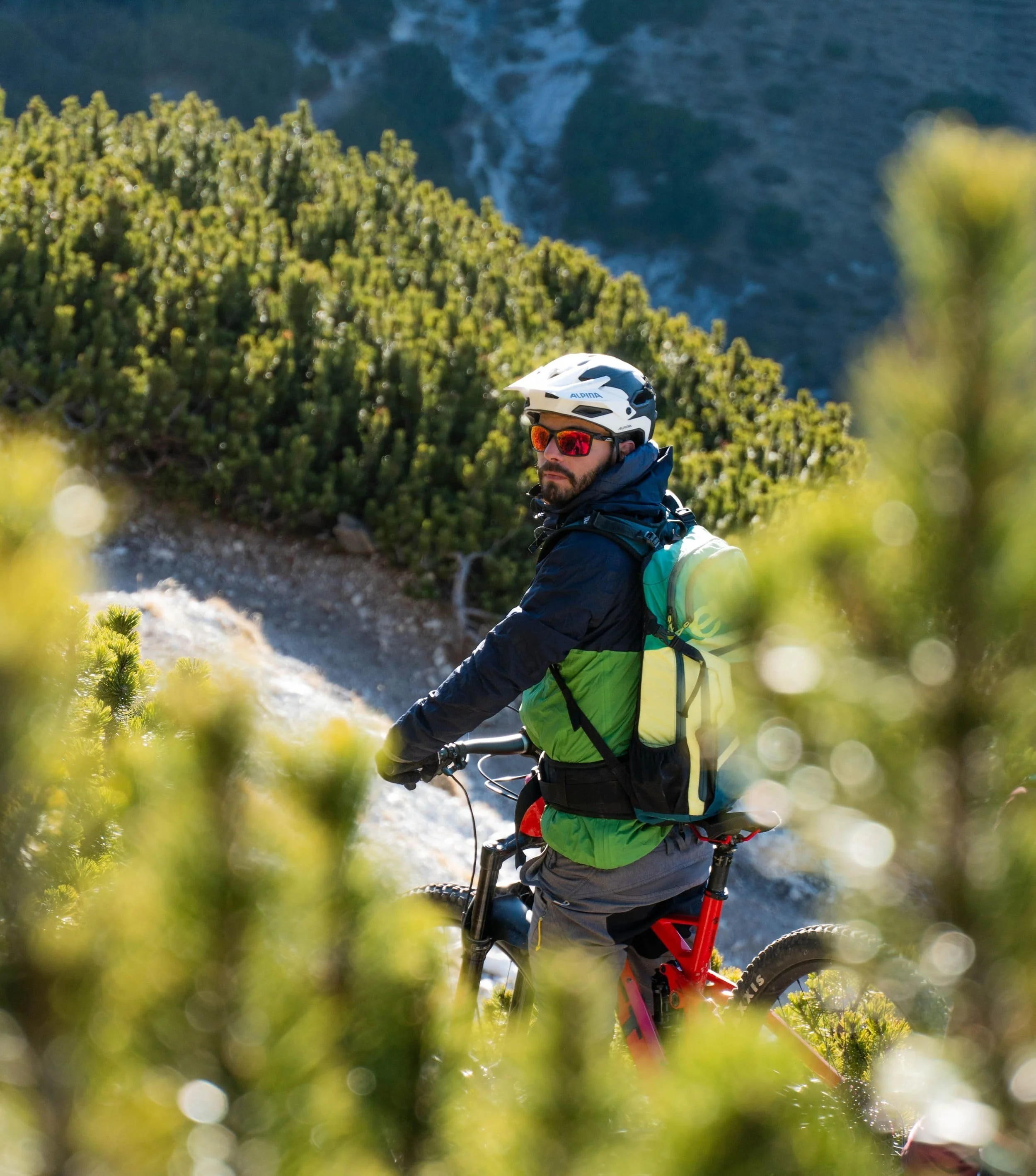 Ein Mountainbiker auf einem Wanderpfad in den Bergen, trägt einen Helm und eine Sonnenbrille.