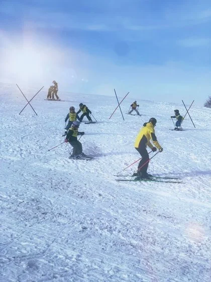 Skifahrer auf einer verschneiten Piste, einige trainieren hinter roten Markierungen.