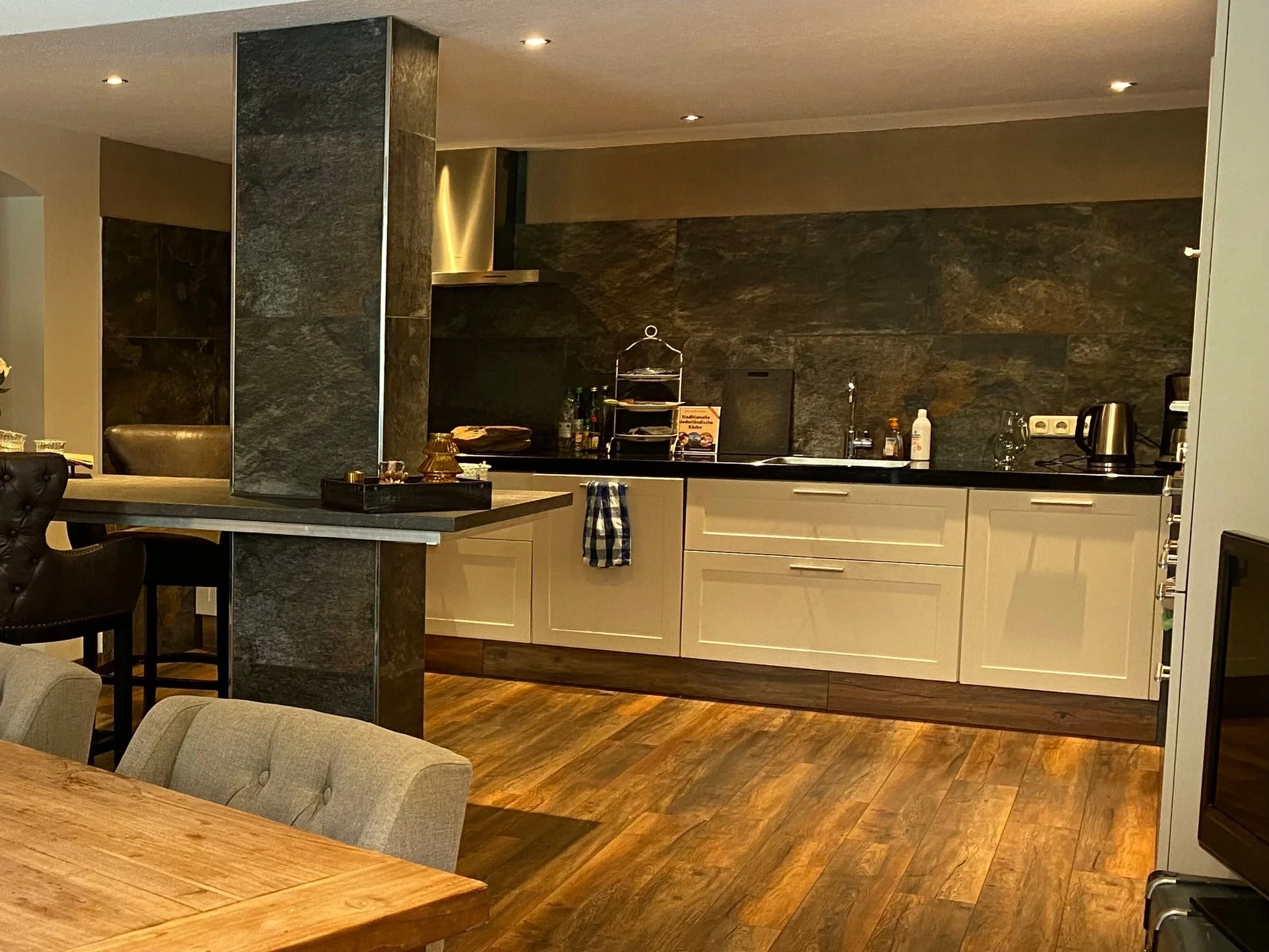 Küche mit weißen Schränken, dunklem Steinwand, Holzboden, Küchenutensilien und Elektrogeräten.