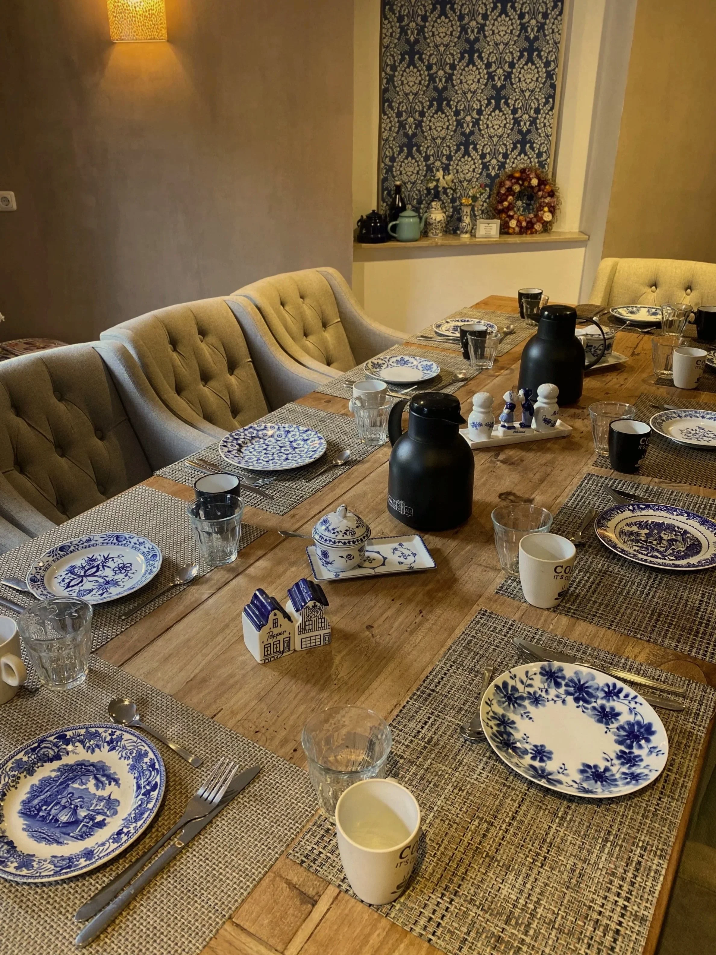 Ein gedeckter Esstisch mit blauen und weißen Geschirr, Gläsern, Tassen, Silberschmuck und schwarzen Thermoskannen in einem Esszimmer.