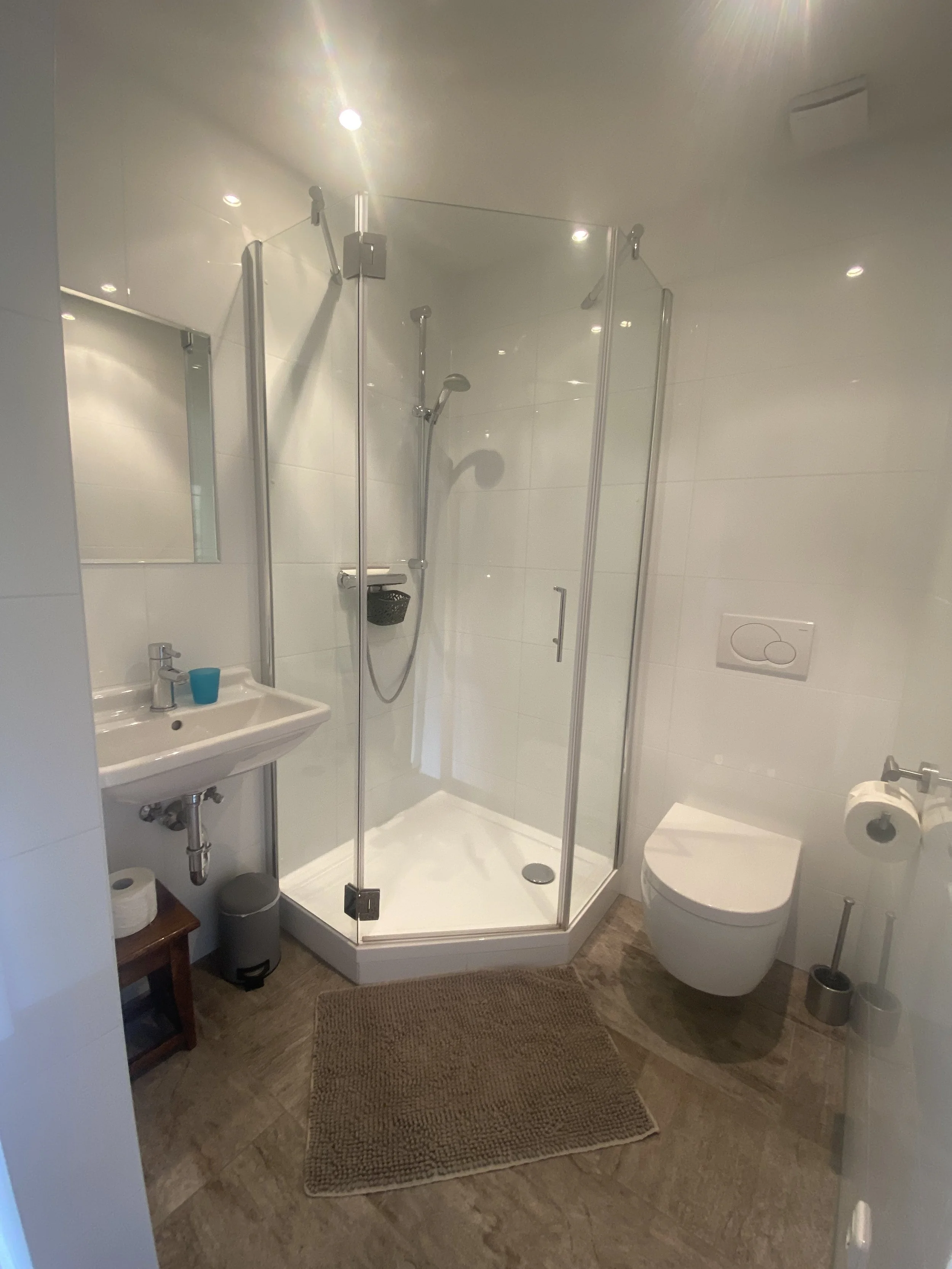 Kleines Badezimmer mit Dusche, WC, Waschbecken, Spiegel und Badematte auf dem Boden.