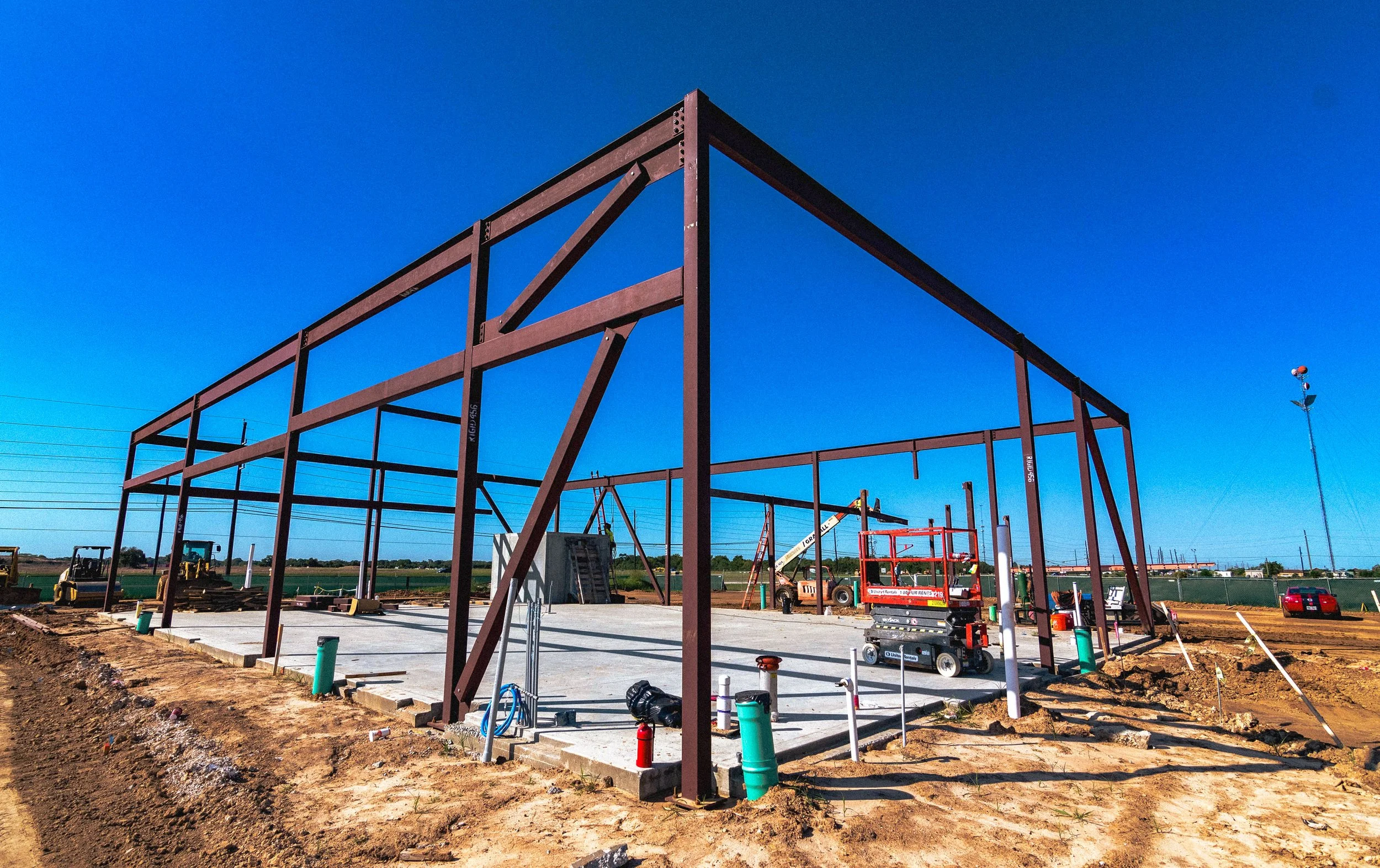 Construction site with steel framework for a building, construction equipment, and tools on a clear, sunny day.