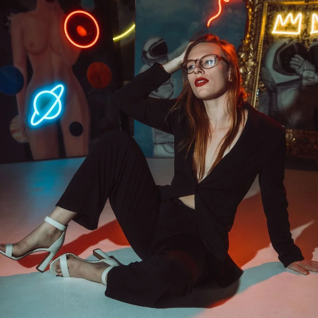 A black and white photograph of a person with shoulder-length hair looking to the side, with colorful lens flare effects.