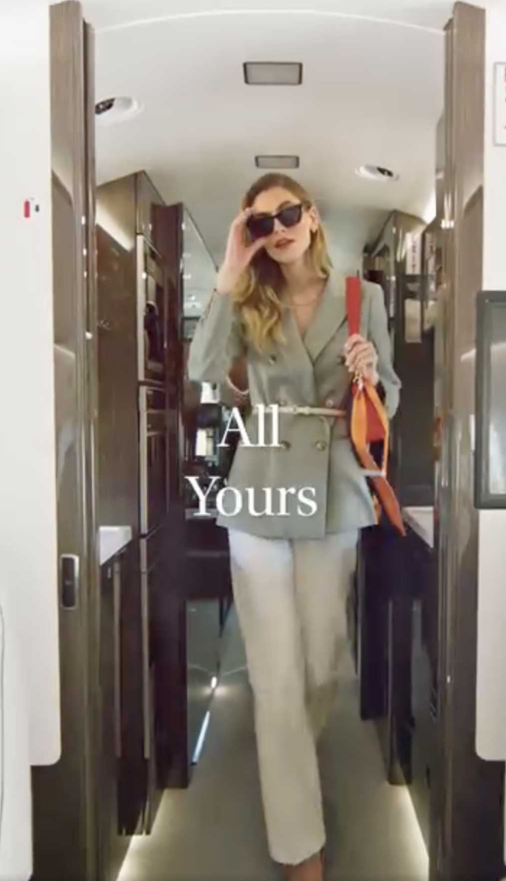 Woman walking down the center of a Gulfstream aircraft cabin, donning sunglasses and preparing to deplane. On-screen text reads: "All Yours."