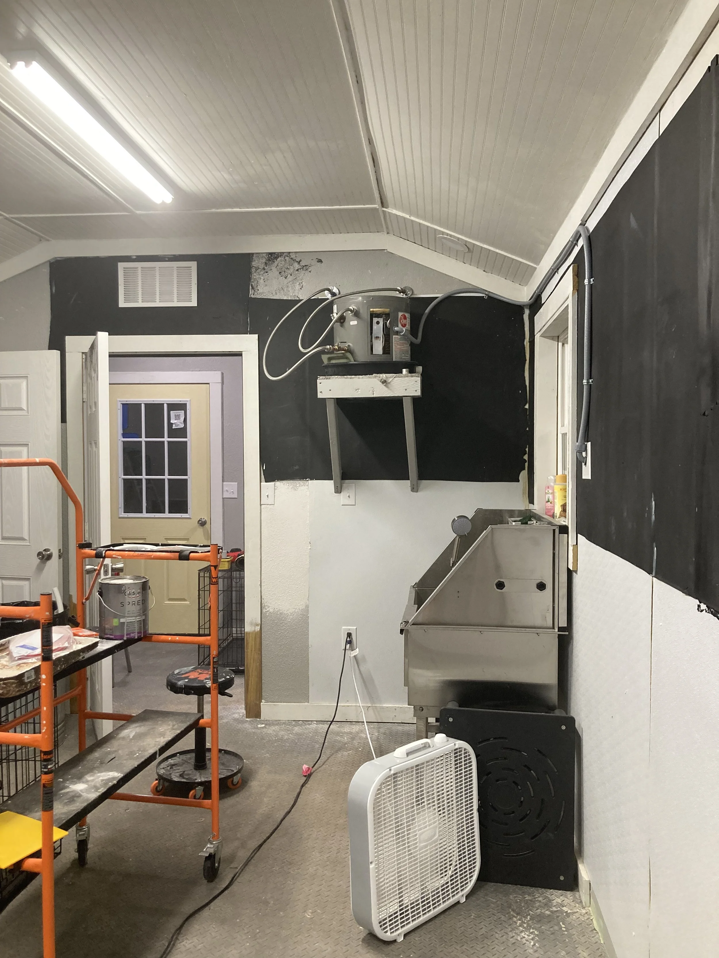 Workshop or kitchen space with industrial equipment, including a metal meat grinder, fan, and cash register, with shelves, tables, and cleaning supplies.
