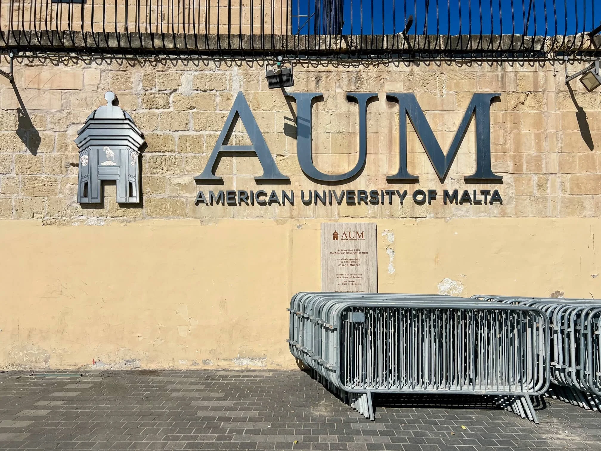 Close-up of the American University of Malta AUM logo sign on the red brick wall.