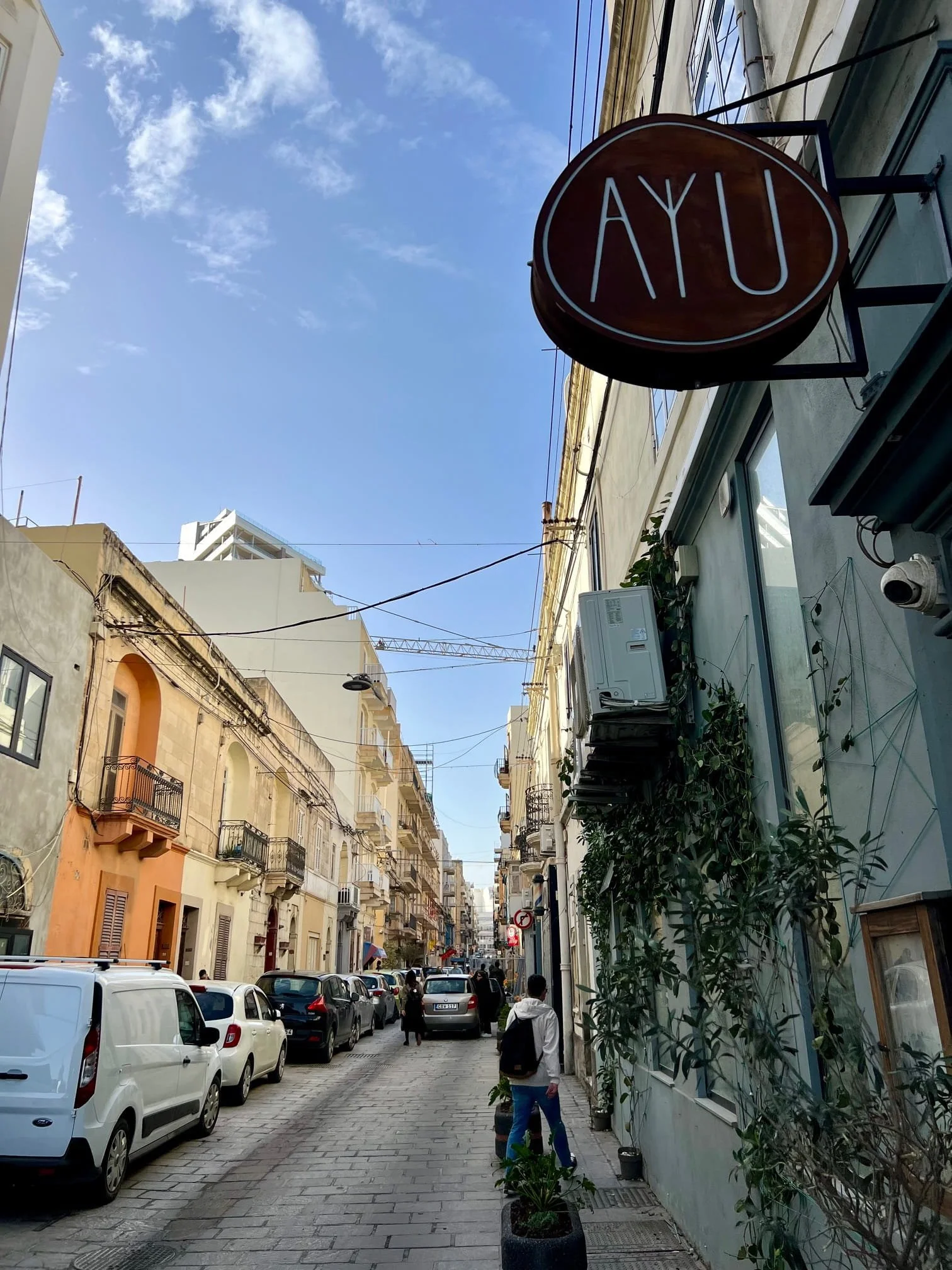 A typical narrow street in Gzira (Triq Manoel de Vilhena) with traditional stone buildings, parked cars and the sign of "Ayubowan" restaurant.