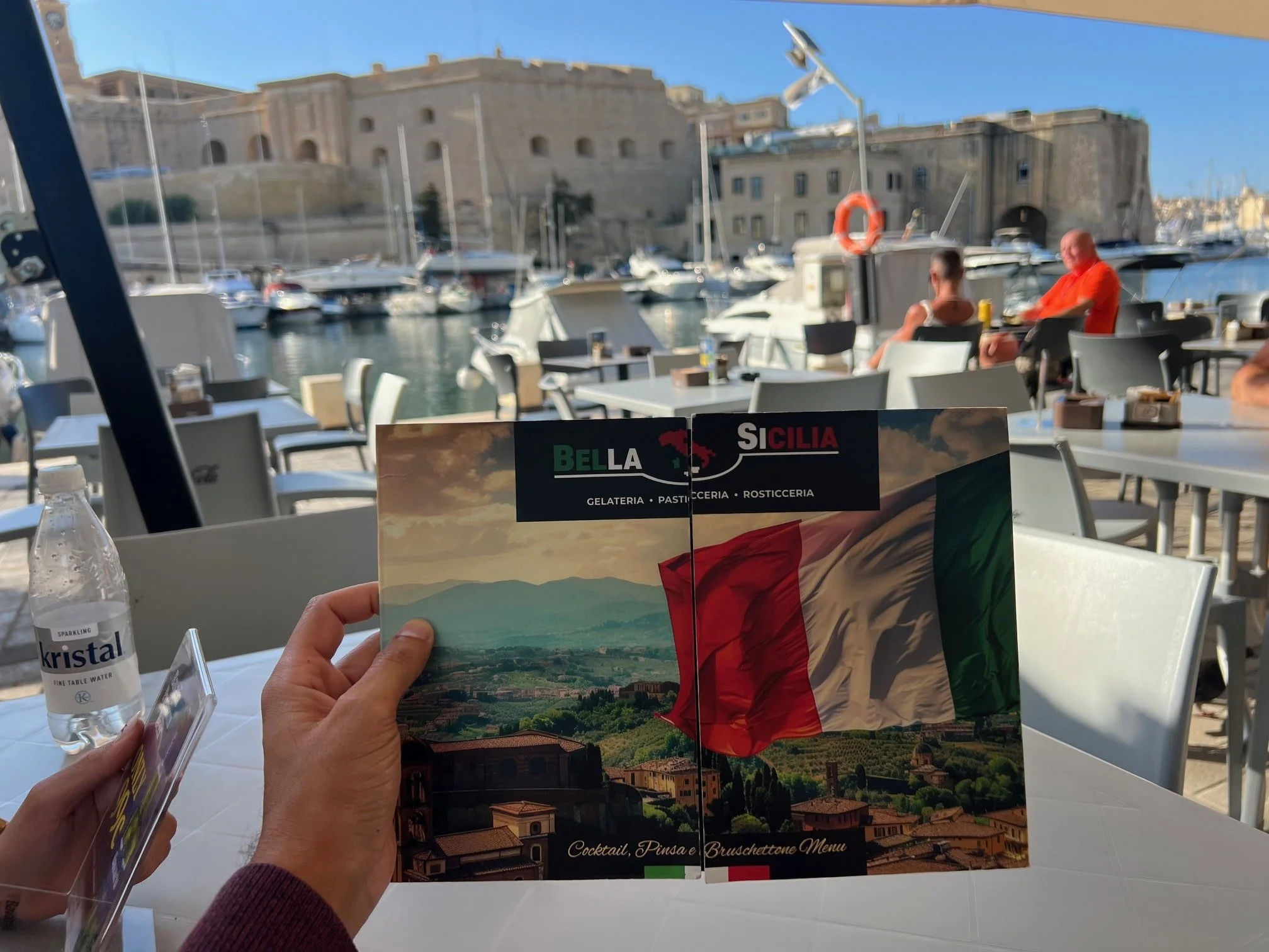 Menu card at Bella Sicilia café in Cospicua with a view of the marina boats.