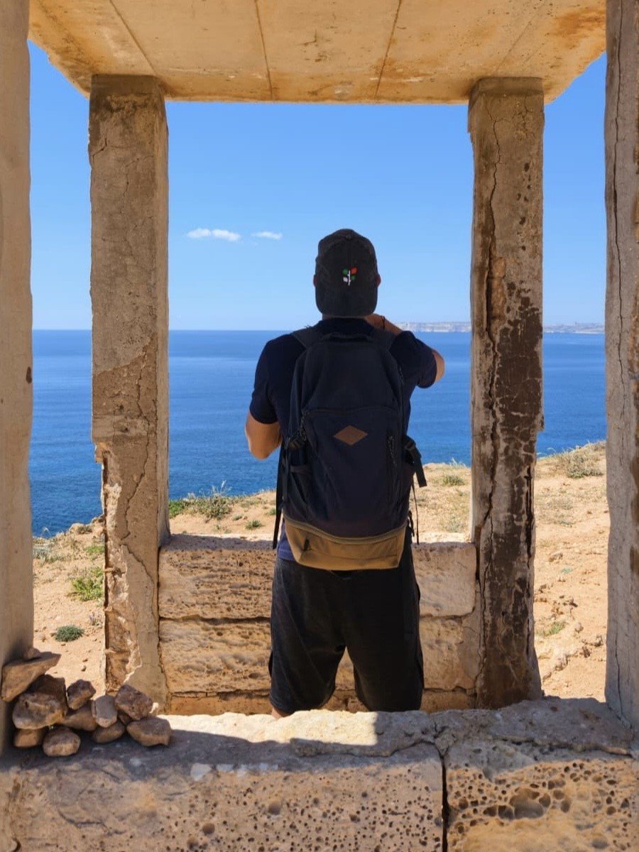 Eroded limestone rock formation framing a person looking out at the sea in Il-Majjistral Park.